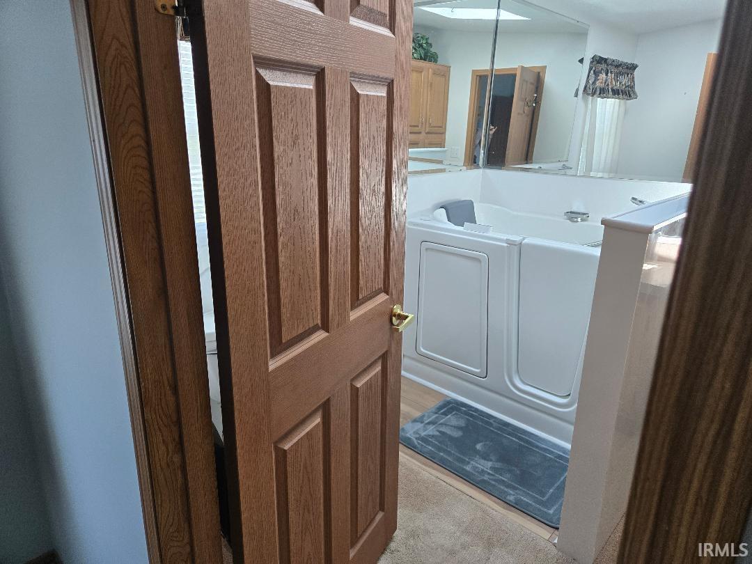 Bathroom featuring a white walk-in tub with a built-in seat, wood-finish flooring, and a partial wall with a mirrored surface