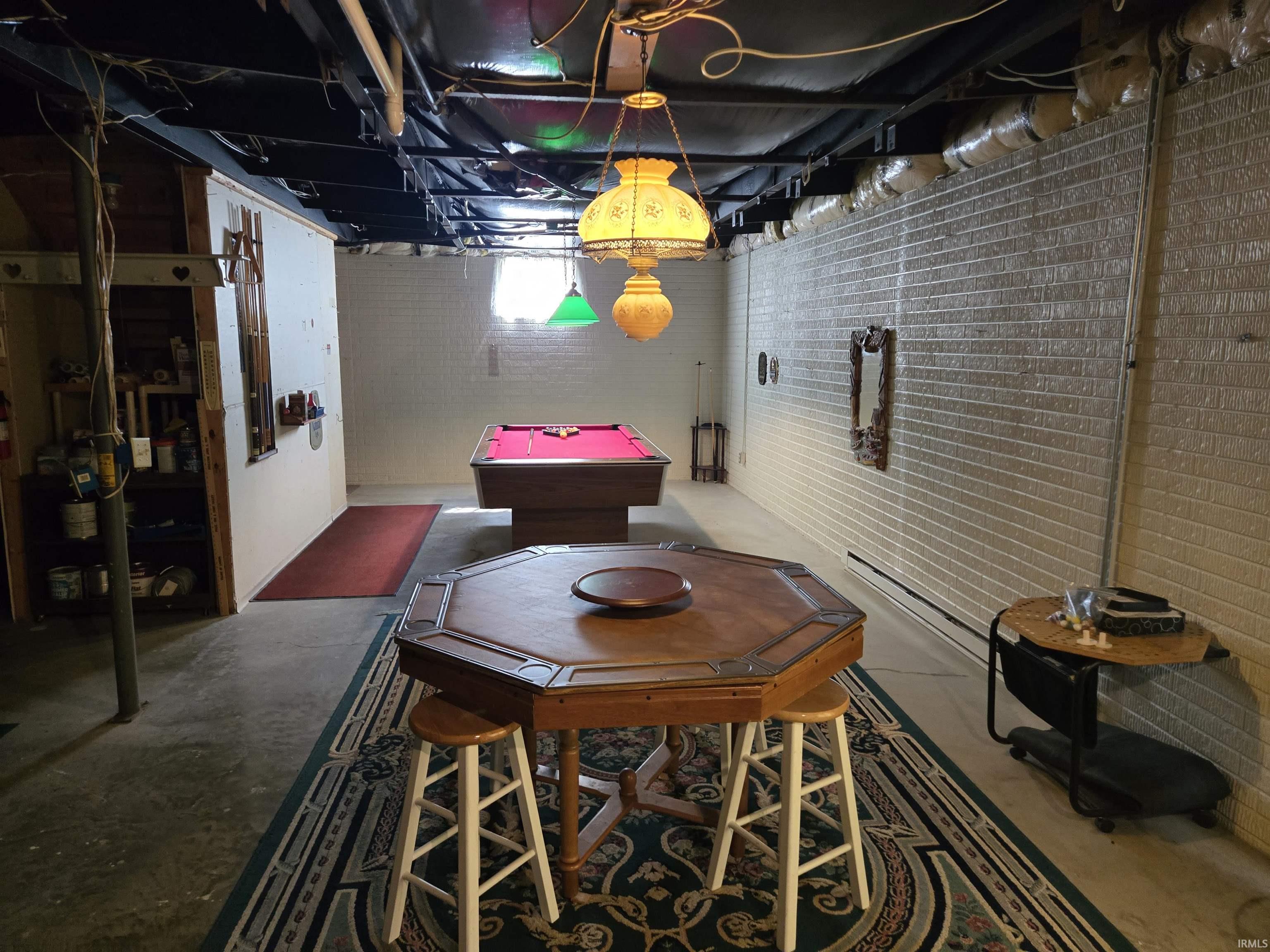 Recreation space featuring a wood-finish octagon table with stools, exposed ceiling joists, and painted brick walls