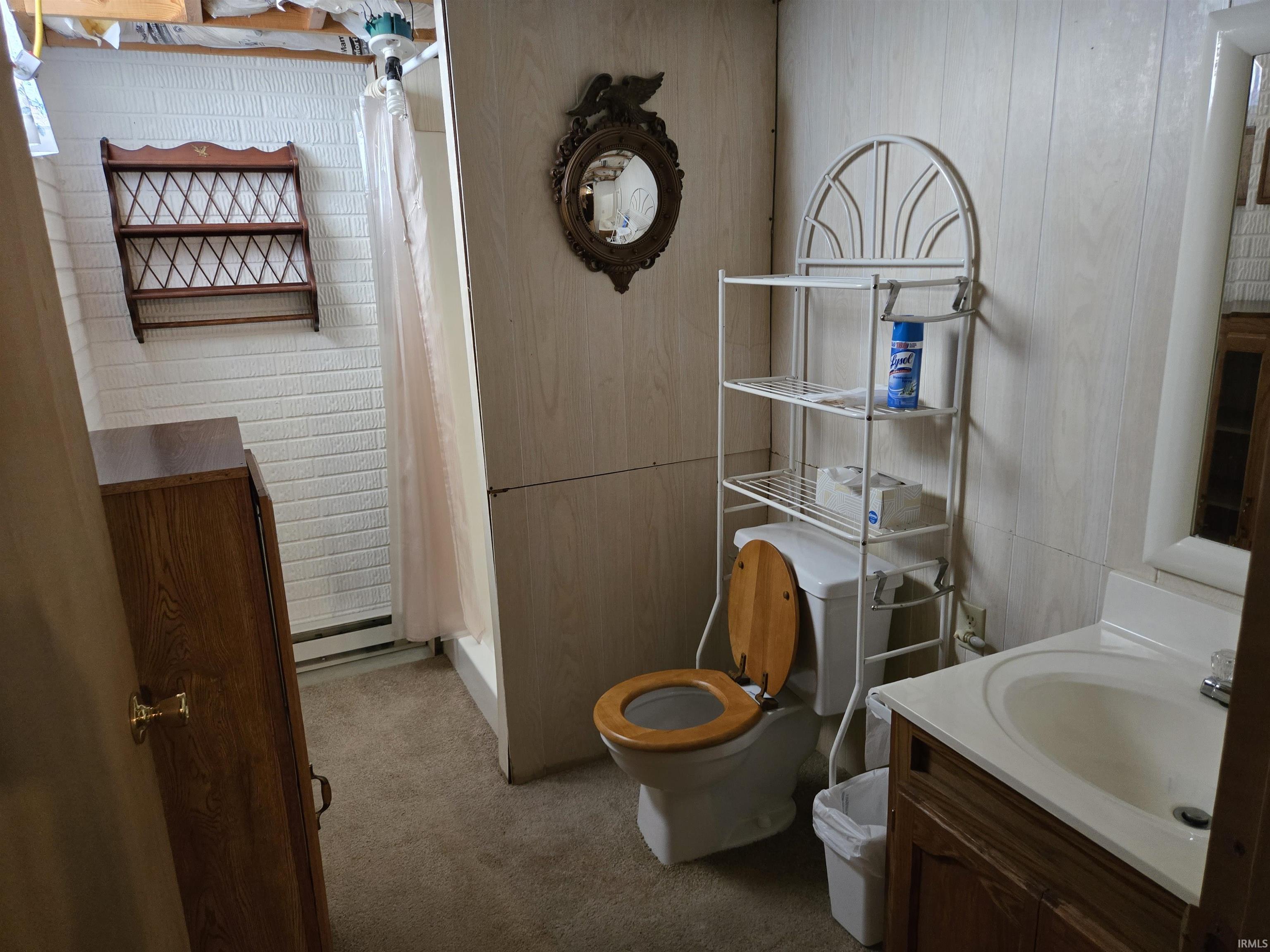 Bathroom featuring wood-finish paneling, a single vanity with an integrated sink, a toilet with a wooden seat, and a shower stall with a privacy curtain