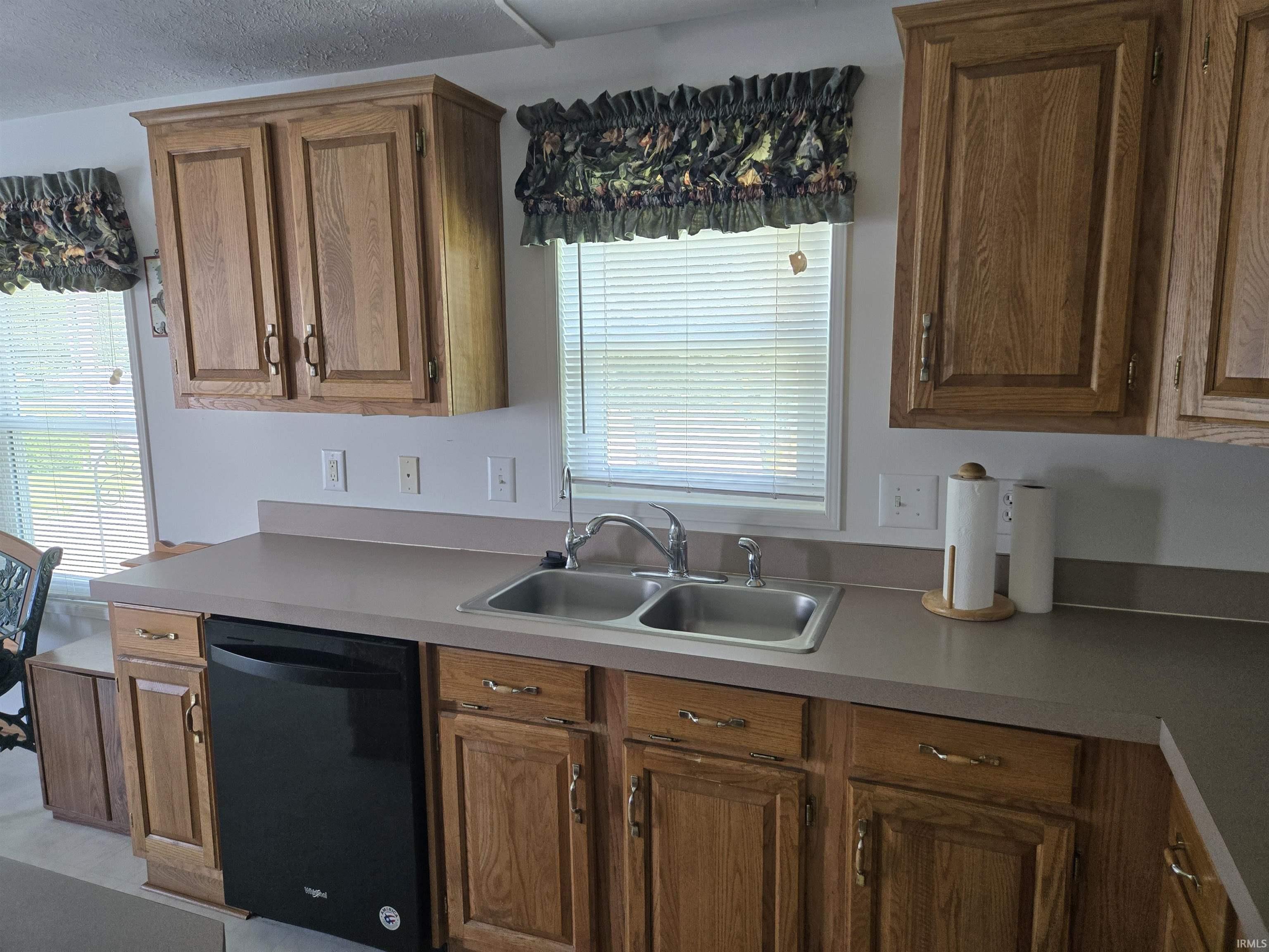Kitchen featuring wood-finish cabinetry, a double basin stainless steel sink, solid surface countertops, and a black built-in dishwasher