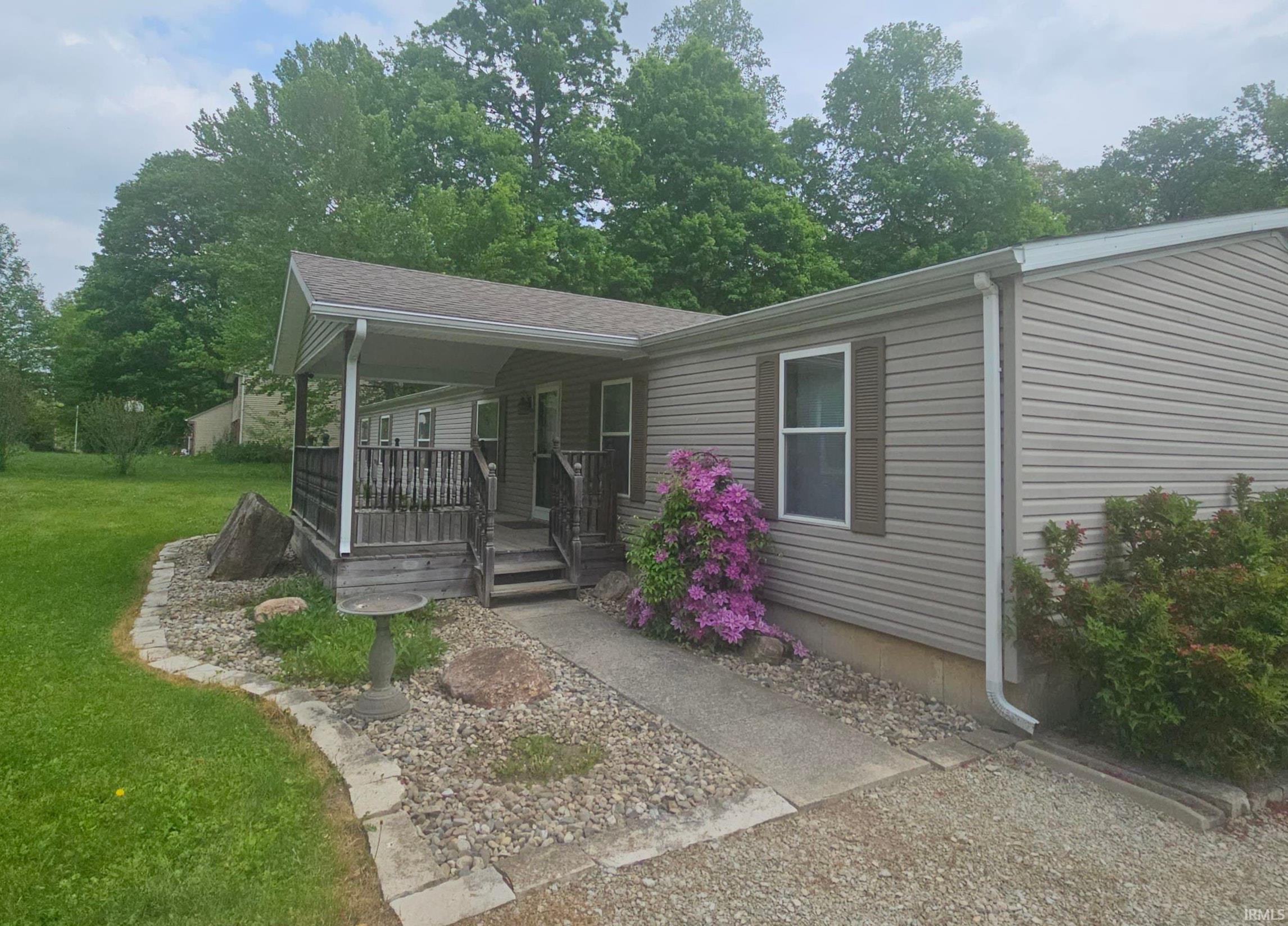 Exterior featuring a covered porch, vinyl siding, shuttered window, concrete walkway, and gravel landscaping