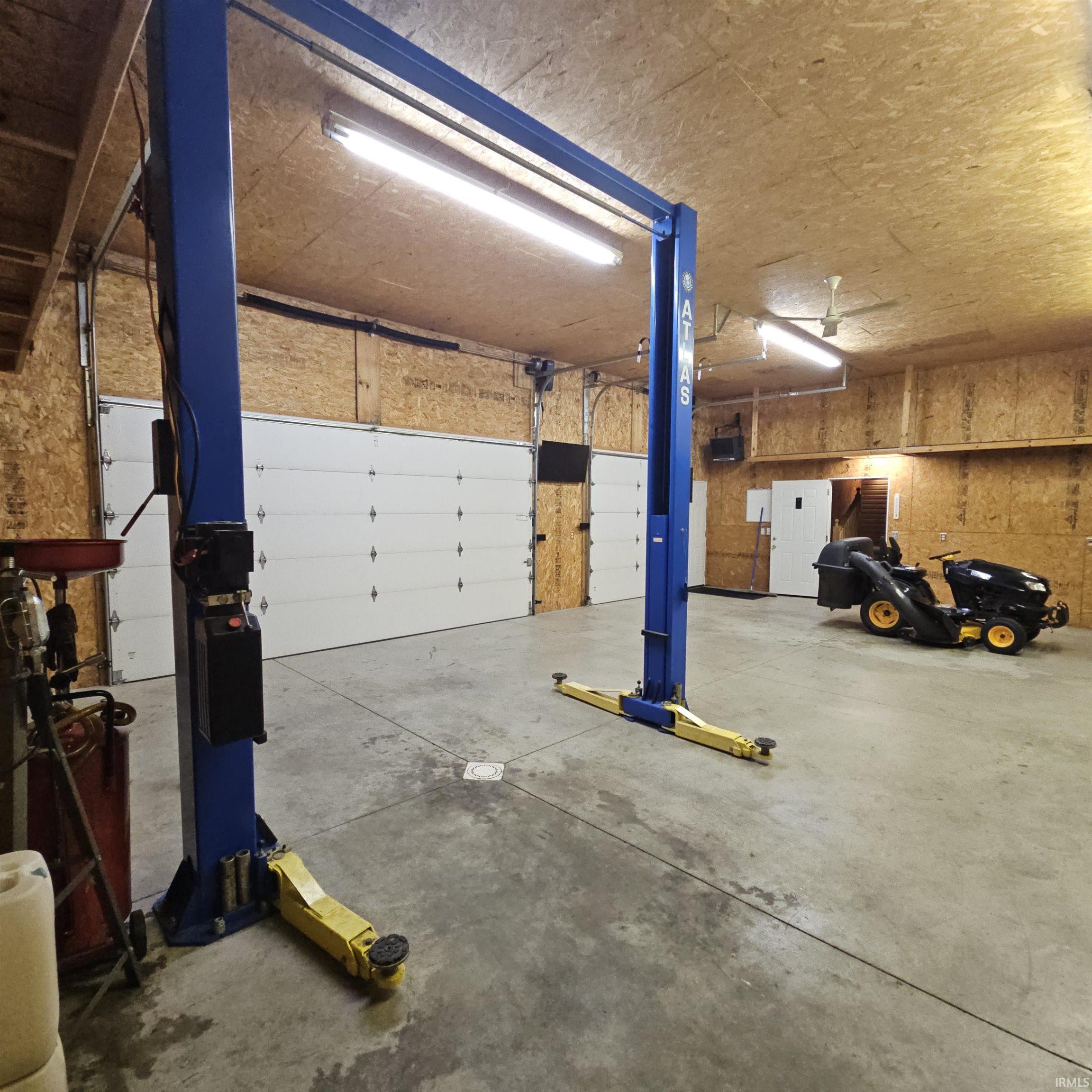 Spacious garage featuring a two-post vehicle lift, concrete flooring, and multiple overhead fluorescent light fixtures