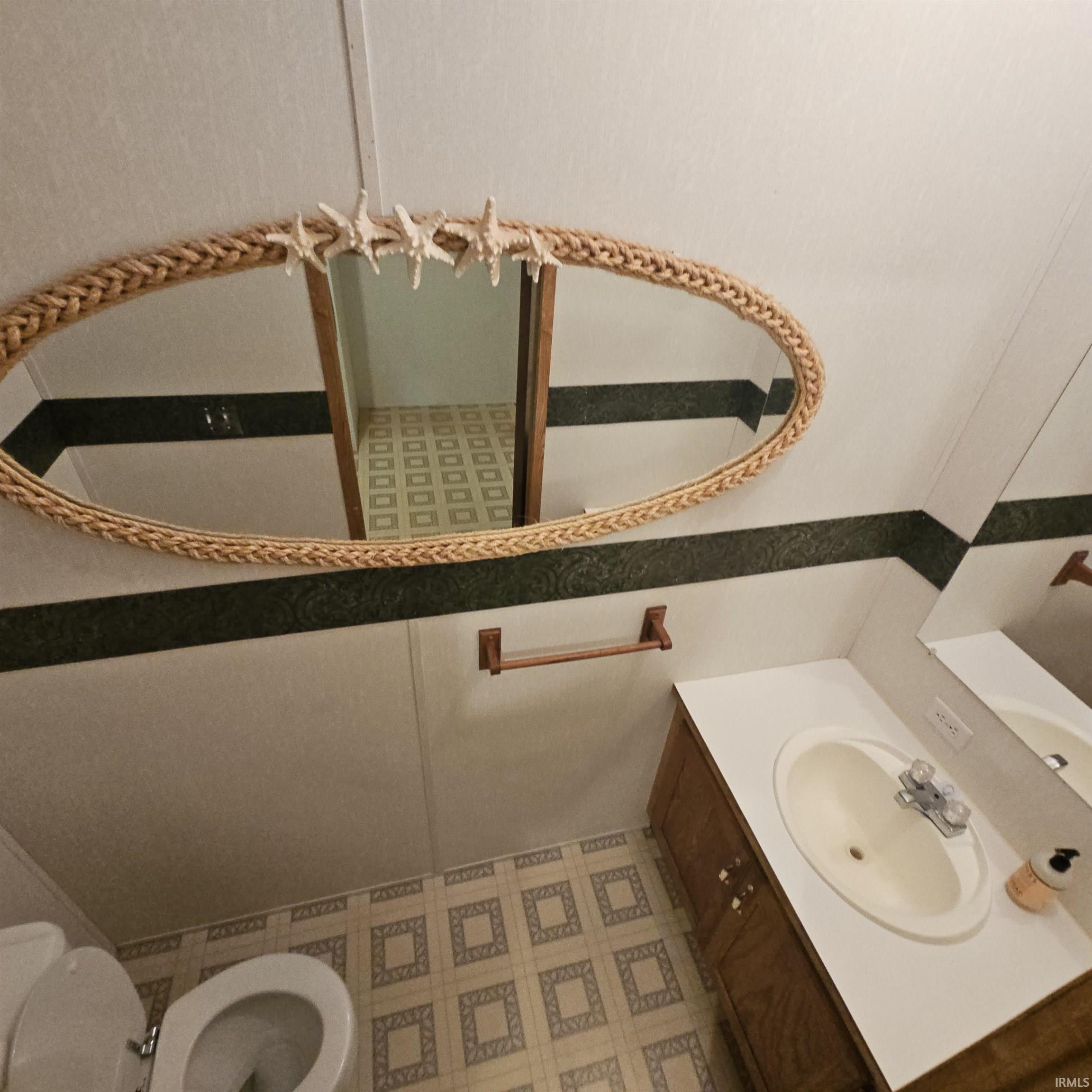Bathroom featuring an oval mirror with a woven frame, white vanity with an integrated sink, wood-finish cabinet, and patterned flooring