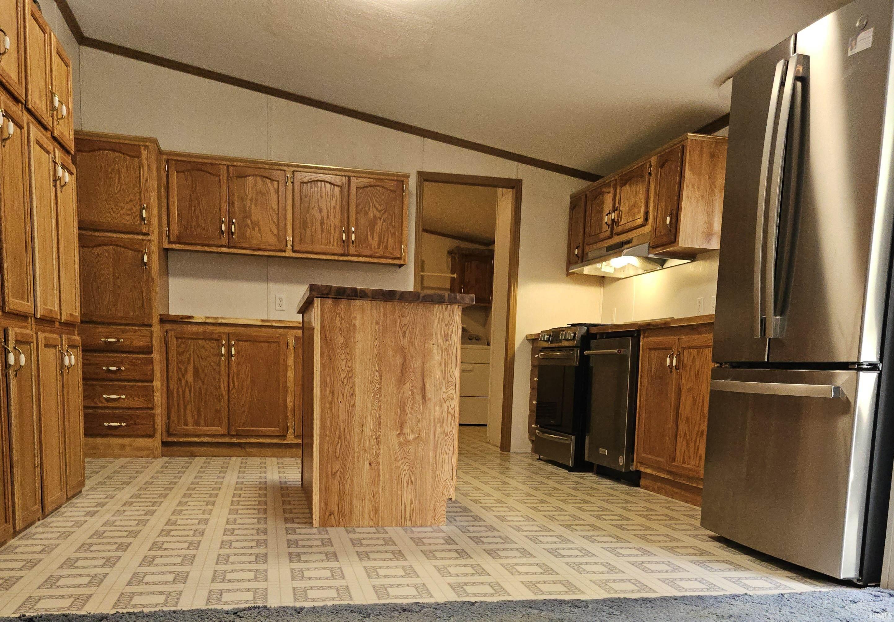 Kitchen featuring ample wood cabinetry, a central island, stainless steel refrigerator, stainless steel oven, and patterned tile flooring
