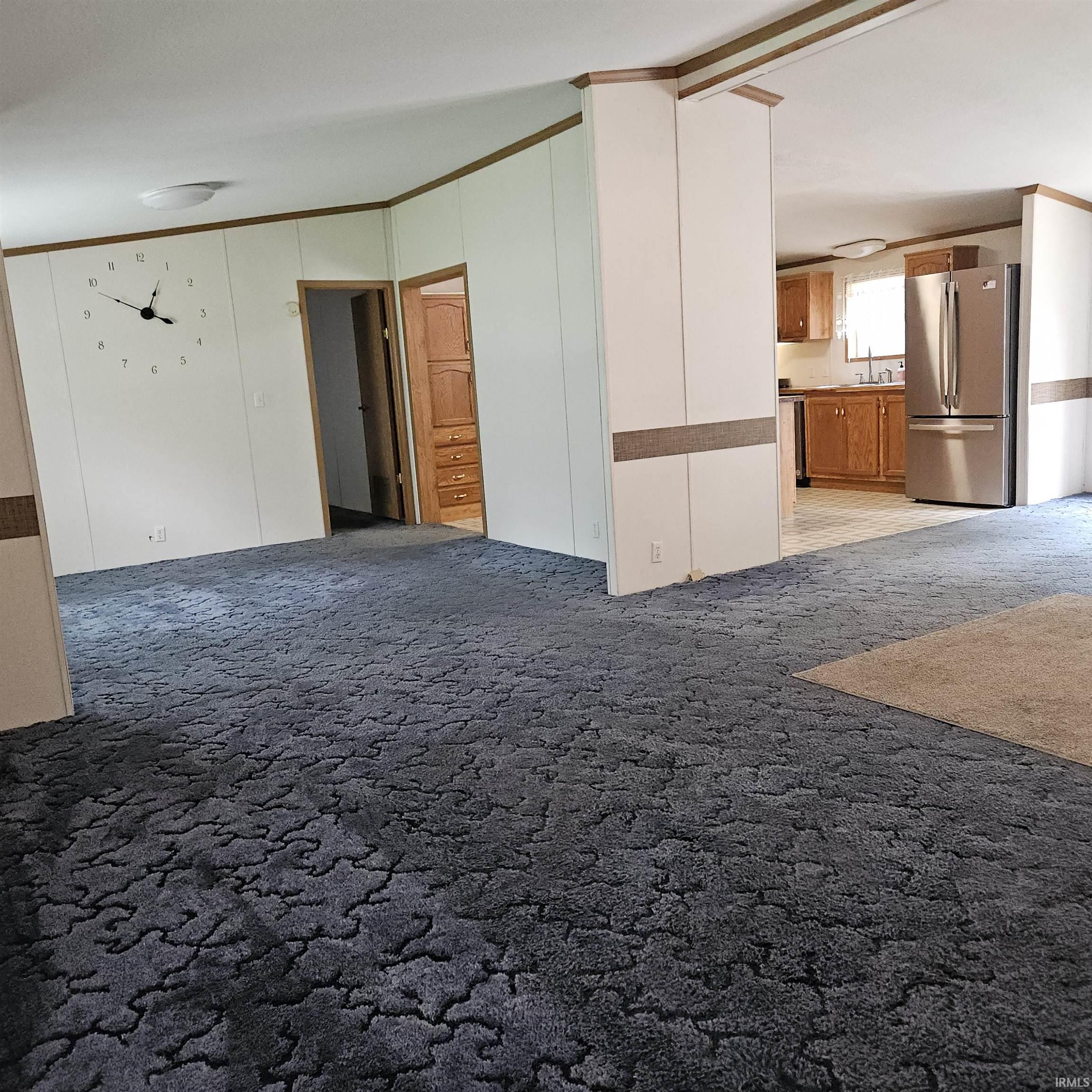 Spacious room featuring patterned carpeting and white panel walls with wood-finish trim
