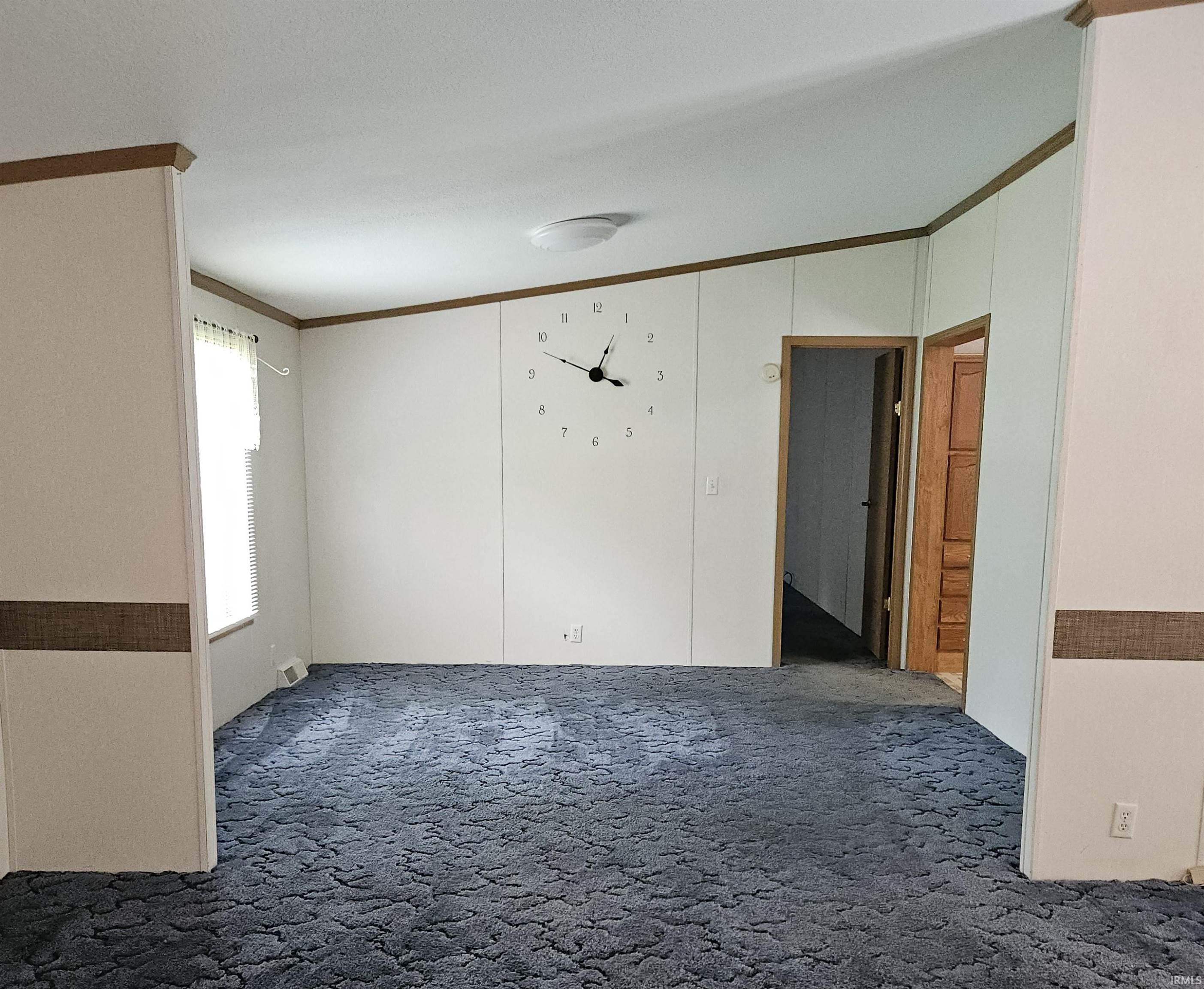 Spacious room featuring blue patterned carpeting, light-toned wall paneling with accent trim, and a window providing natural illumination
