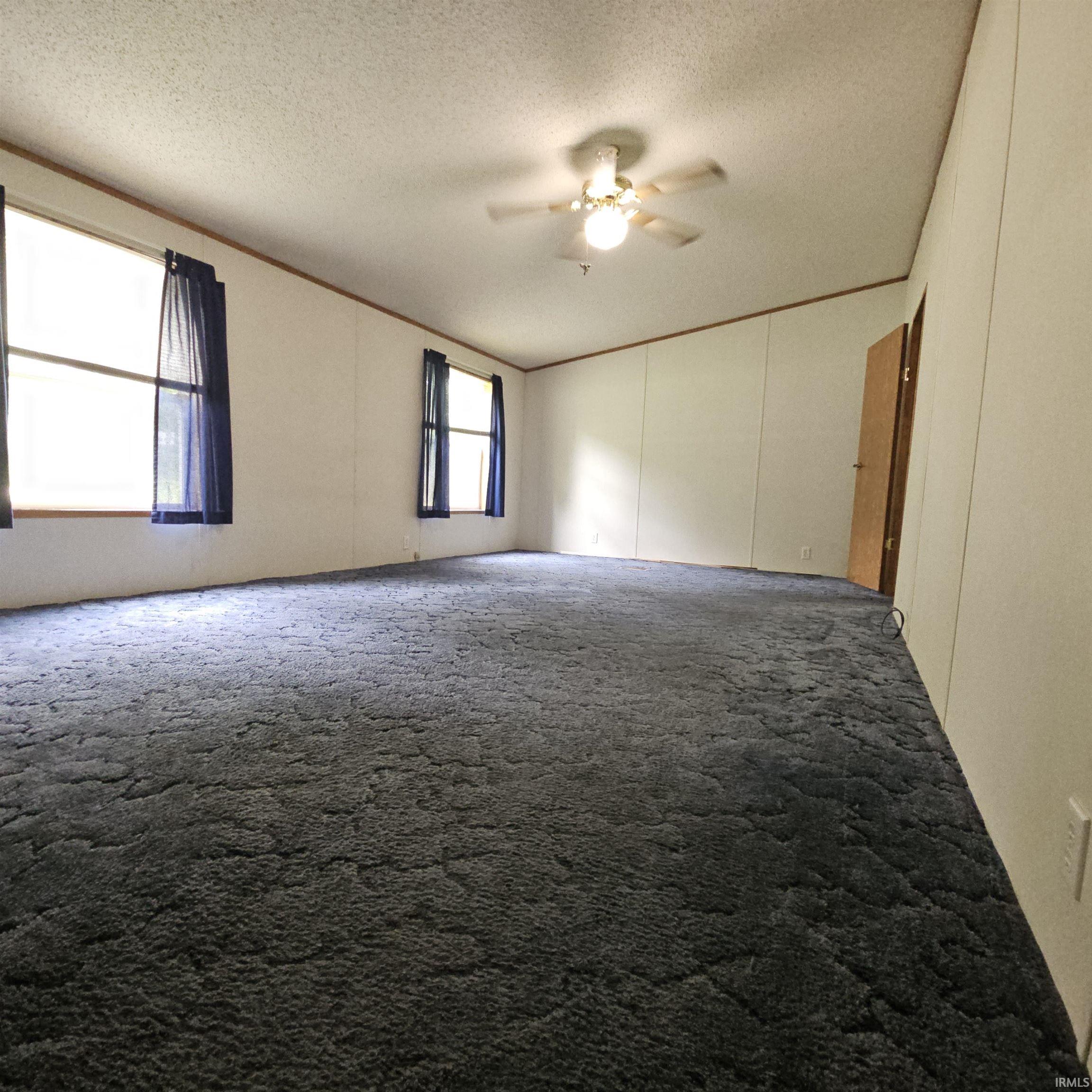 Spacious room featuring plush blue carpeting, multiple windows, a ceiling fan with integrated lighting, and a light-colored interior door