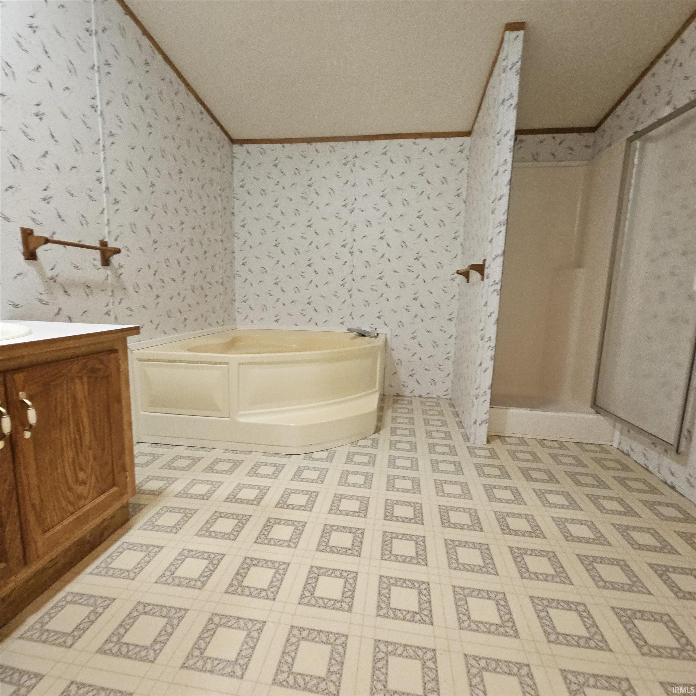 Bathroom featuring a corner soaking tub, a separate shower enclosure, wood-finish vanity with countertop, patterned sheet vinyl flooring, and wallpapered walls