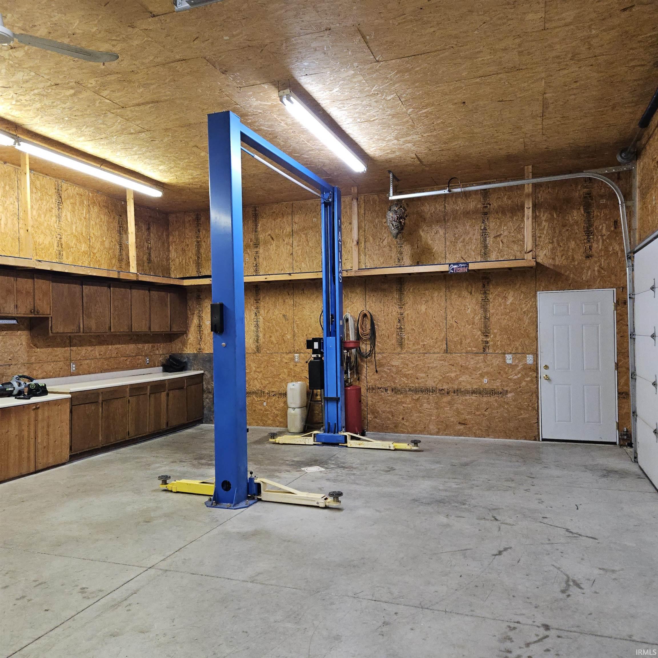 Spacious garage featuring a vehicle lift, concrete flooring, extensive built-in cabinetry, overhead shelving, and bright overhead lighting