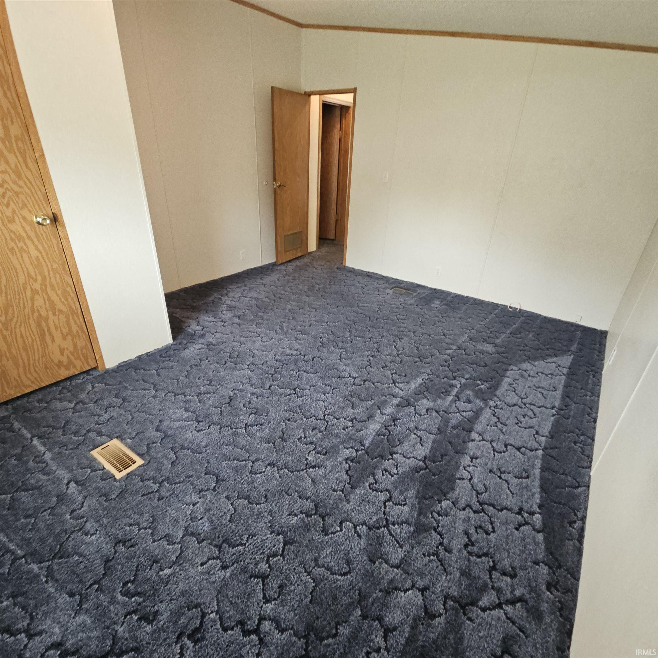 Spacious room featuring patterned blue carpet, light-toned paneling, and two wood-finish doors