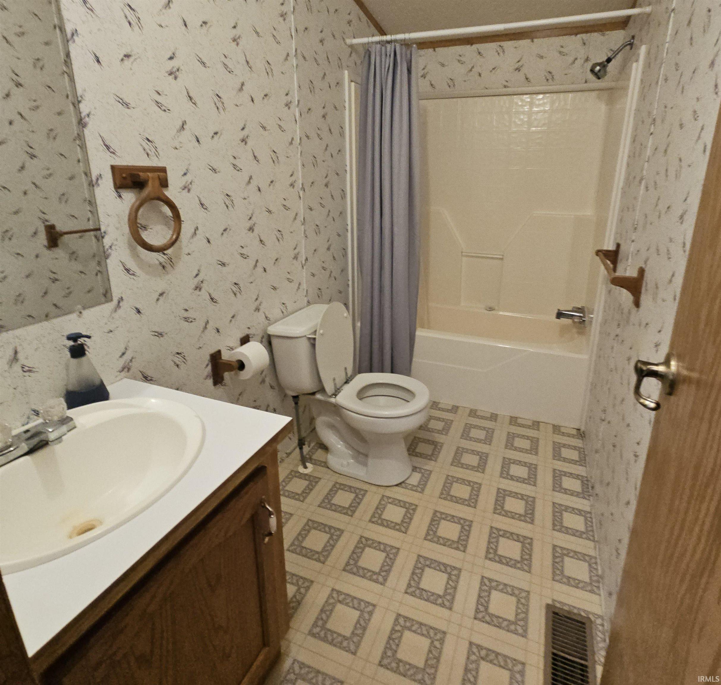 Bathroom featuring a vanity with an integrated sink, a commode, and a tub-shower combination with a shower curtain rod