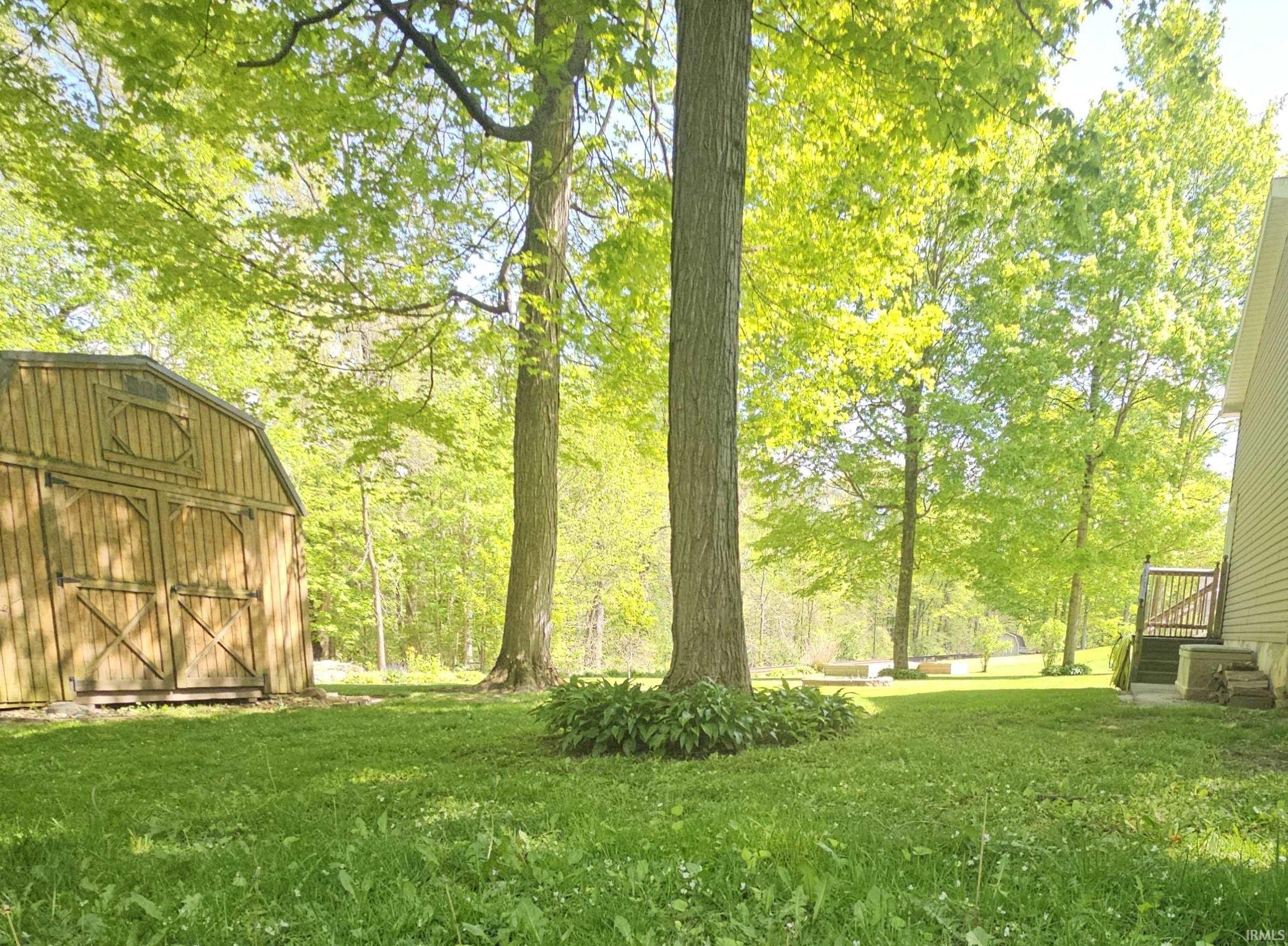 Expansive green lawn with mature trees, a wooden storage shed, and a property exterior featuring horizontal siding and an exterior staircase