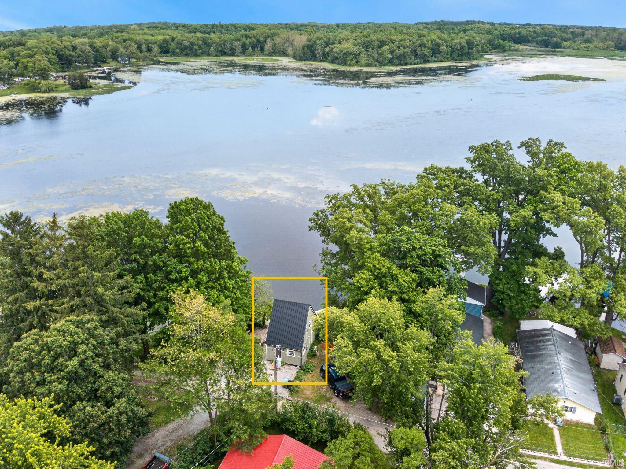 Waterfront property featuring a pitched roofline, light-colored siding, and mature tree coverage