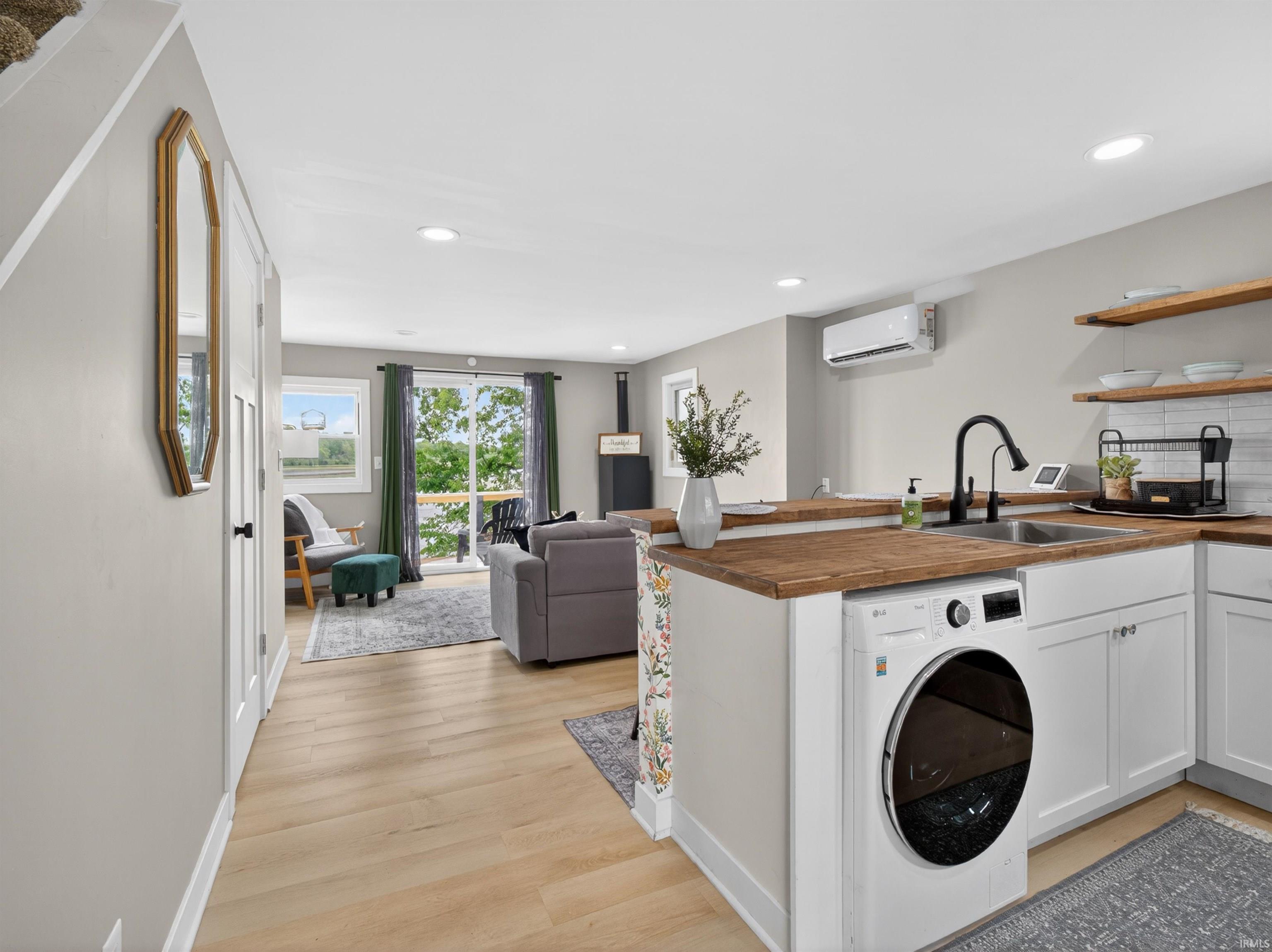 Kitchenette featuring wood-finish countertops, white cabinetry, integrated laundry appliance, stainless steel sink with matte black faucet, and open shelving