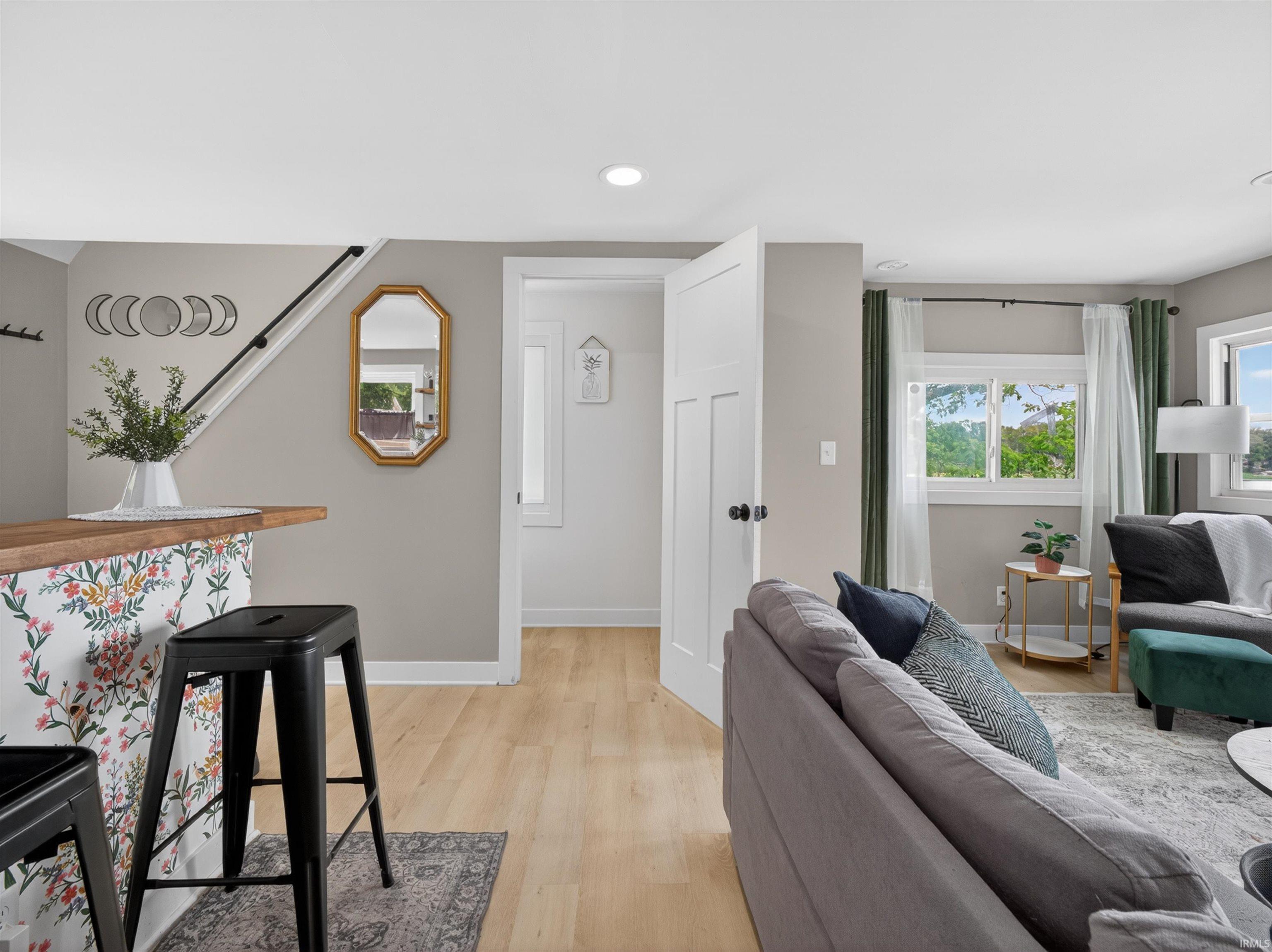Open living area featuring light wood-finish flooring, recessed lighting, and a partial staircase with a black handrail