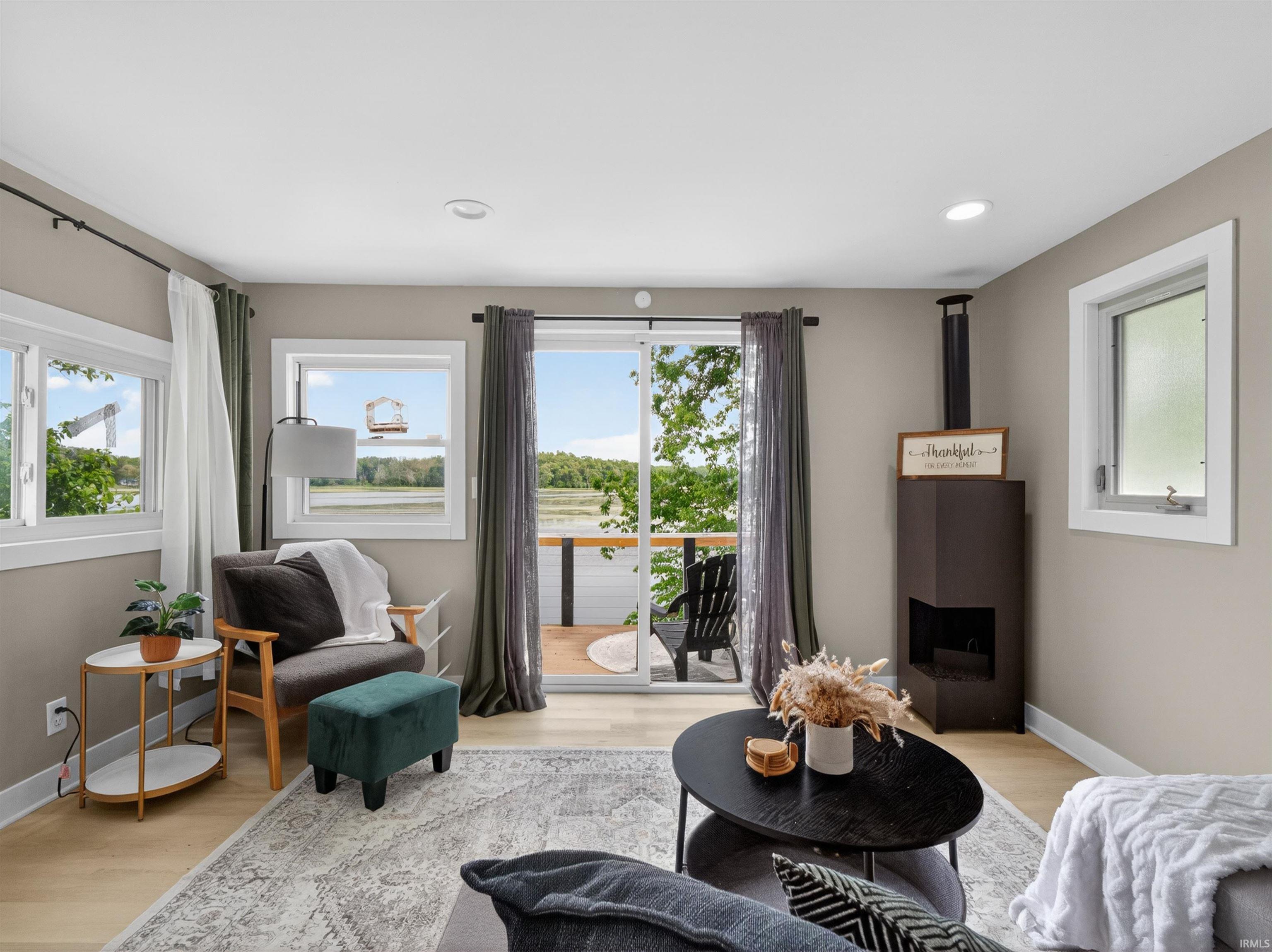 Bright interior space with light-tone wood-finish flooring, a contemporary corner fireplace, and recessed lighting