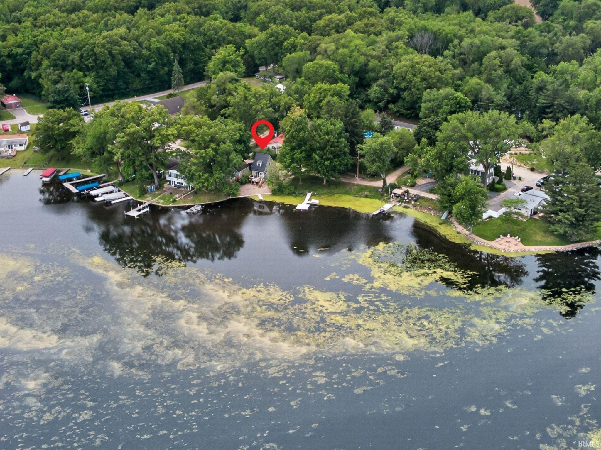 Waterfront property featuring a private dock, expansive green space, mature trees, and a paved driveway