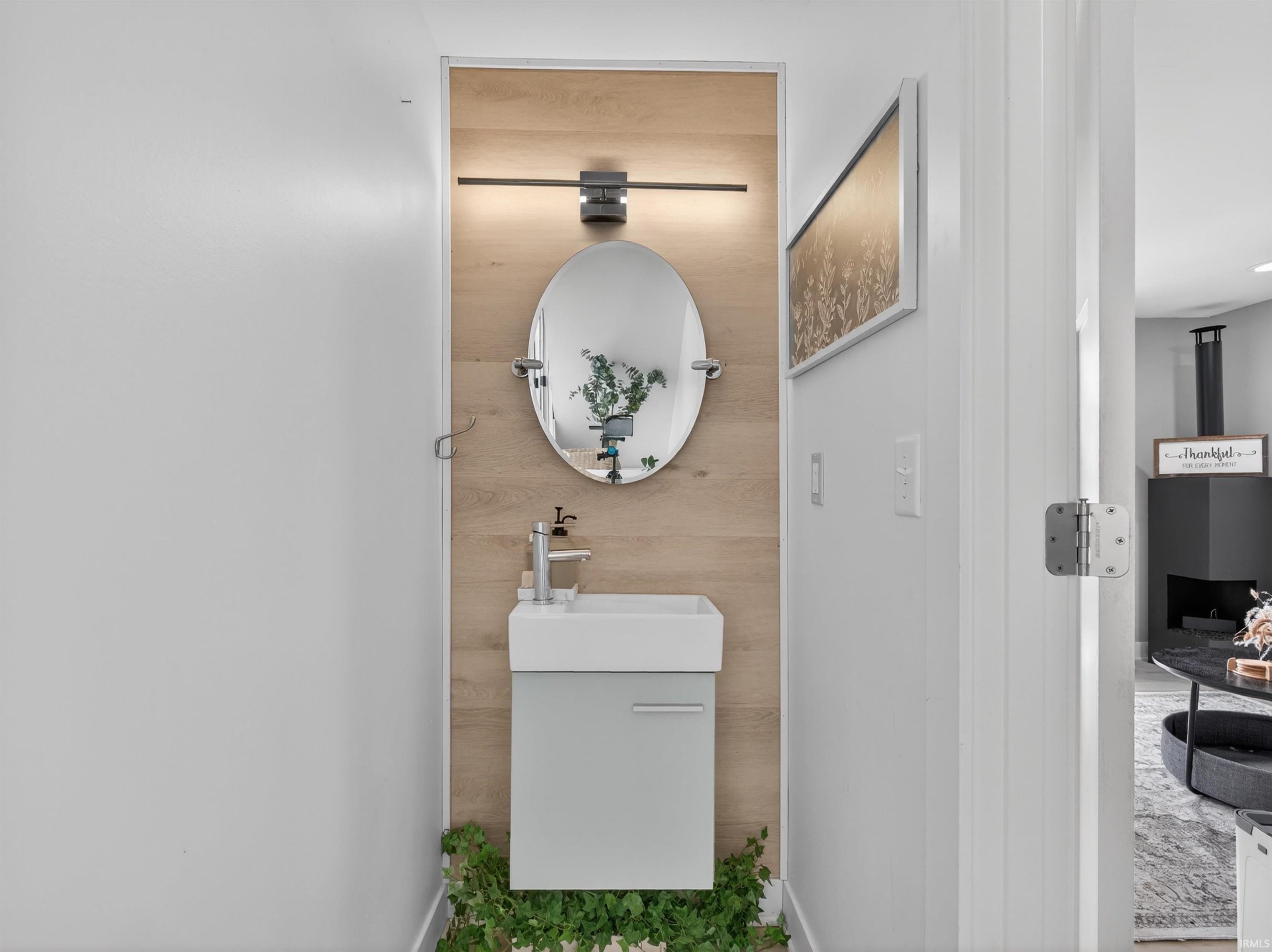 Powder room featuring a wall-mounted vanity with integrated sink, wood-finish accent wall, oval mirror, and linear sconce lighting