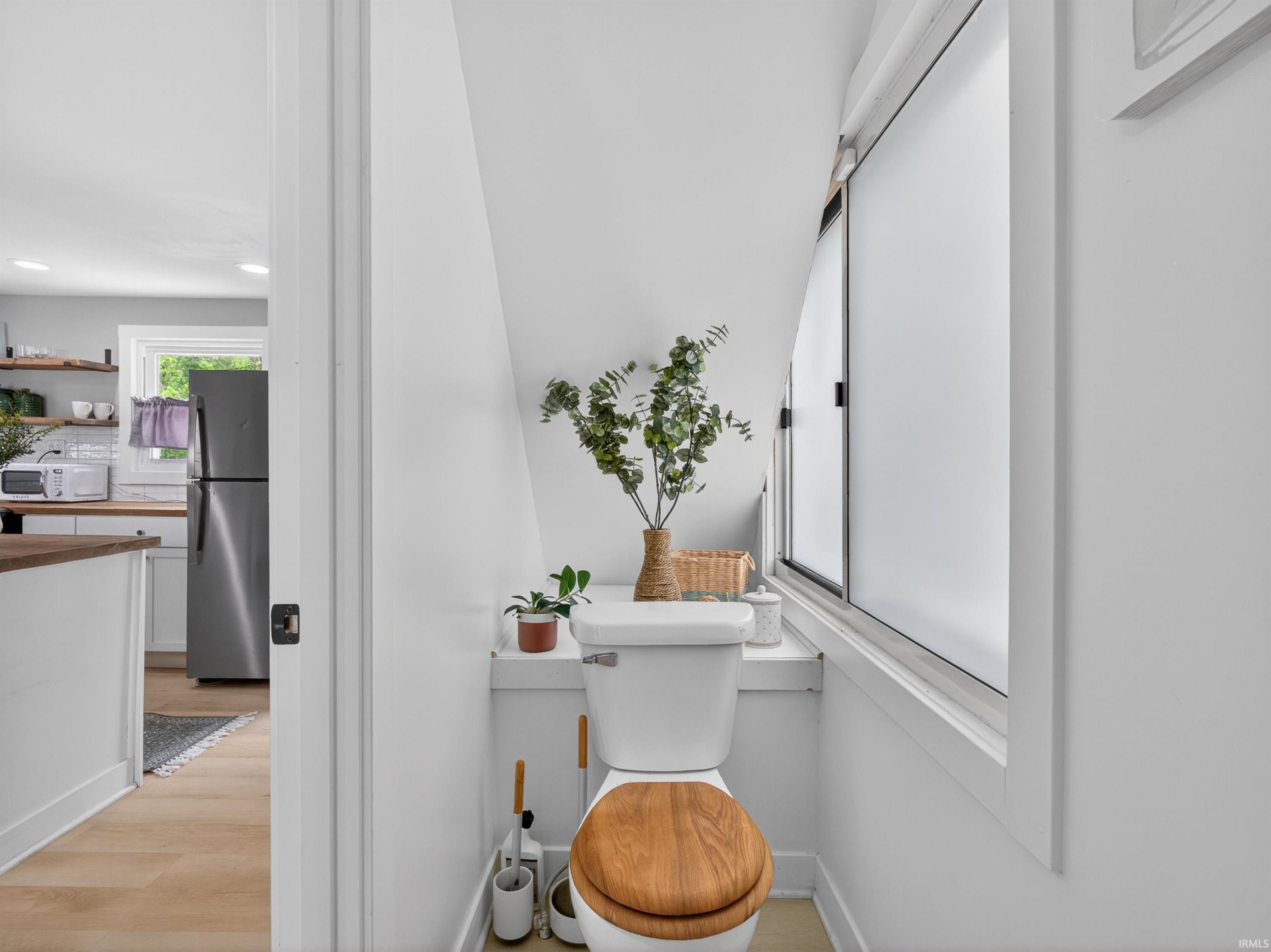 Compact bathroom featuring a white toilet with a wood-finish seat, a frosted window, and a sloped ceiling