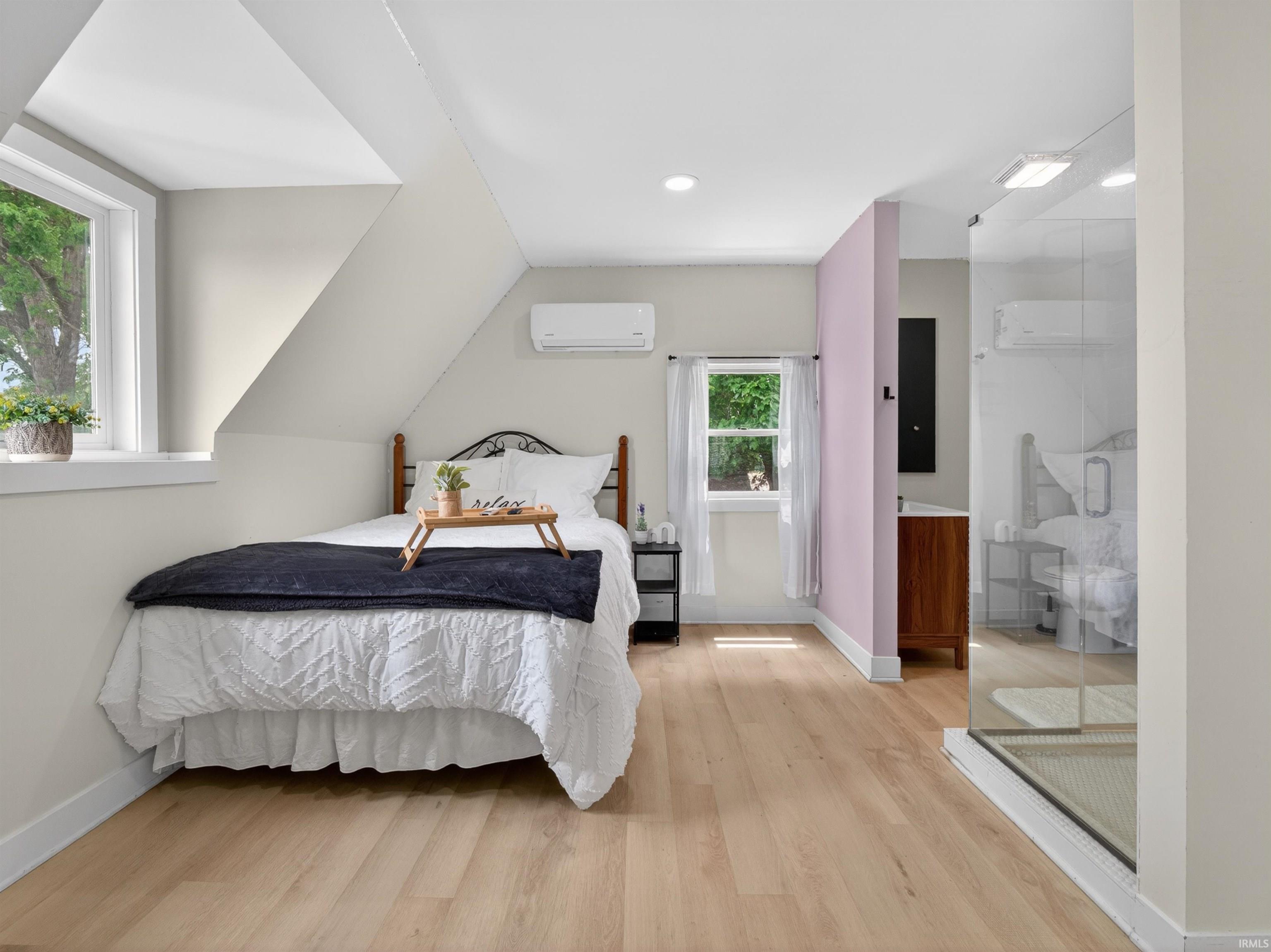 Open-concept room featuring light wood-finish flooring, an angled ceiling, a glass-enclosed shower, a single vanity with wood cabinetry, and a wall-mounted air conditioning unit