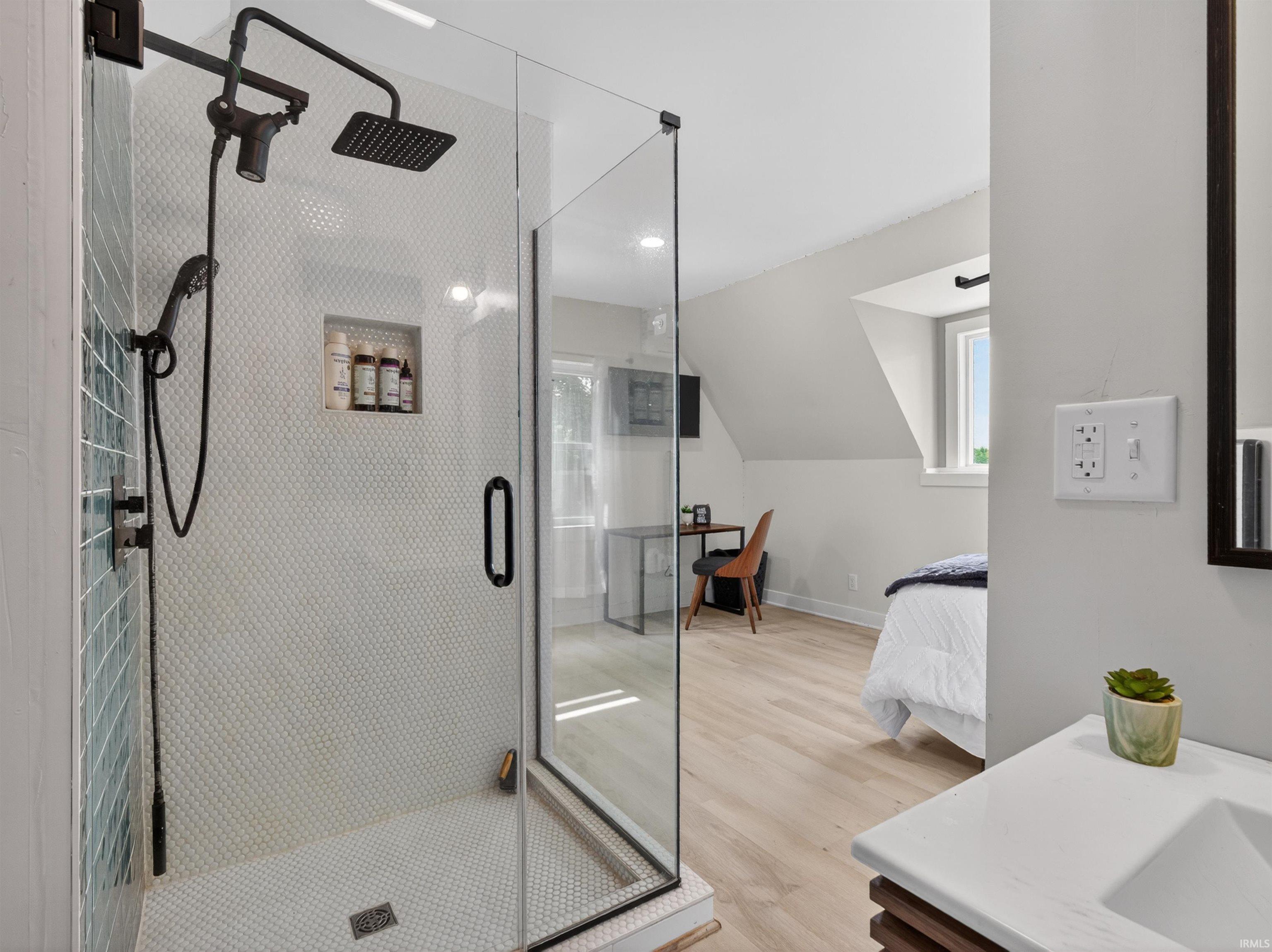 Glass-enclosed shower featuring a rainfall showerhead, handheld shower, and a tiled niche