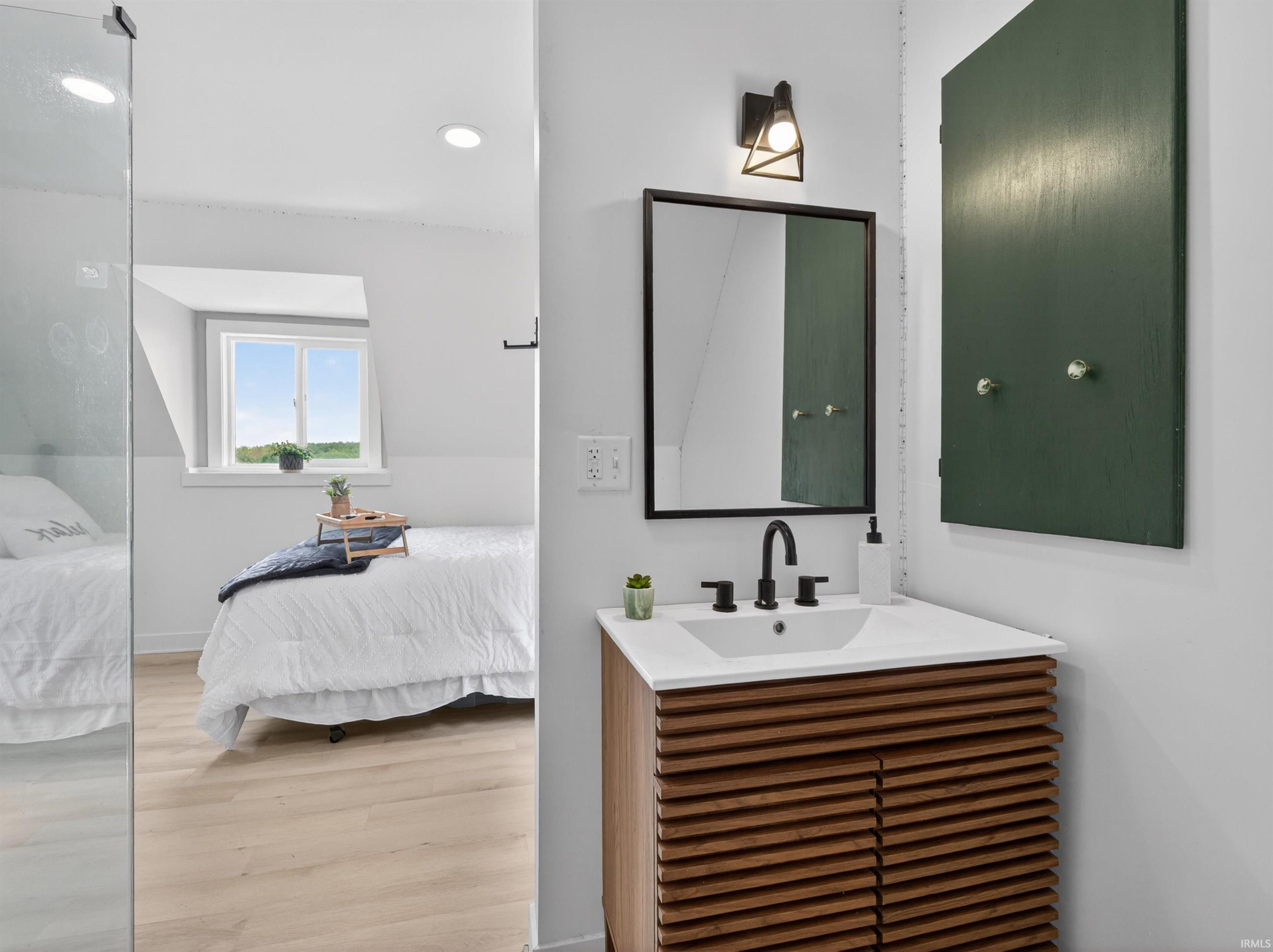 Bathroom vanity featuring a wood-finish cabinet with slatted doors, a white countertop, and a black framed mirror
