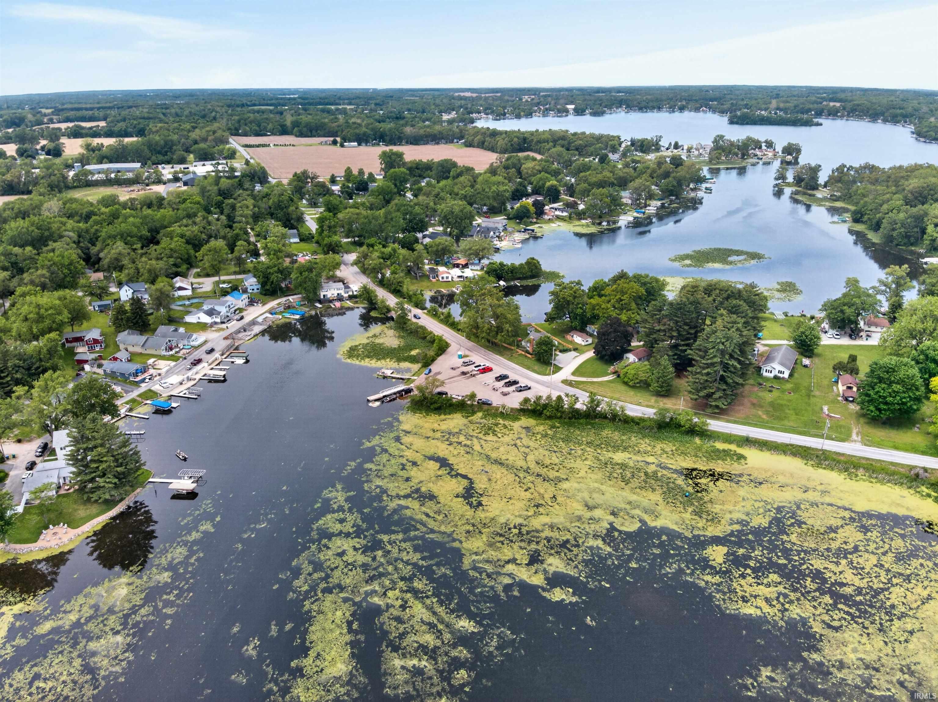Expansive lake setting featuring multiple waterfront properties, docks, surrounding mature trees, and a distant agricultural landscape