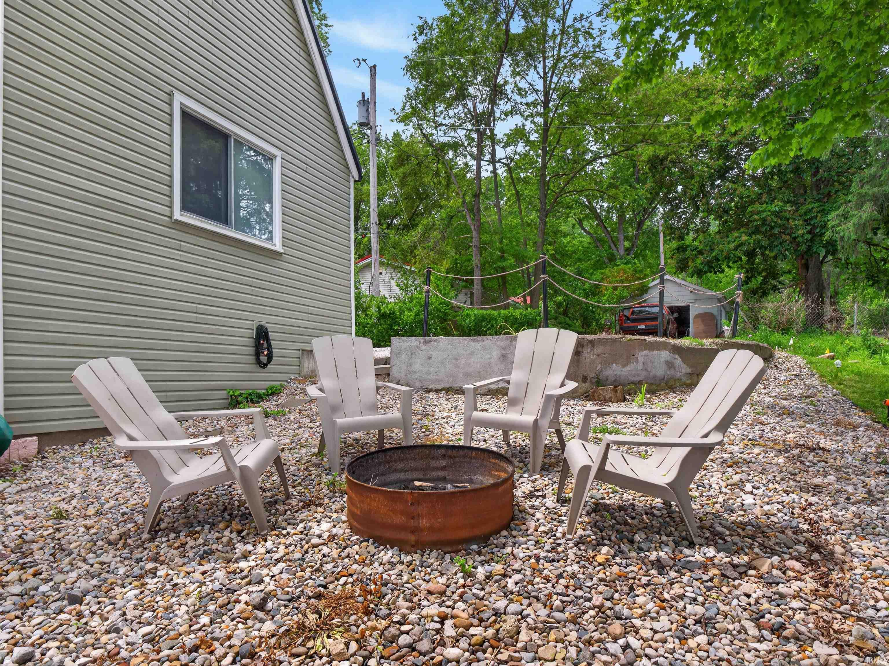 Exterior side yard featuring a fire pit area with gravel ground cover, a utility shed, and mature perimeter trees