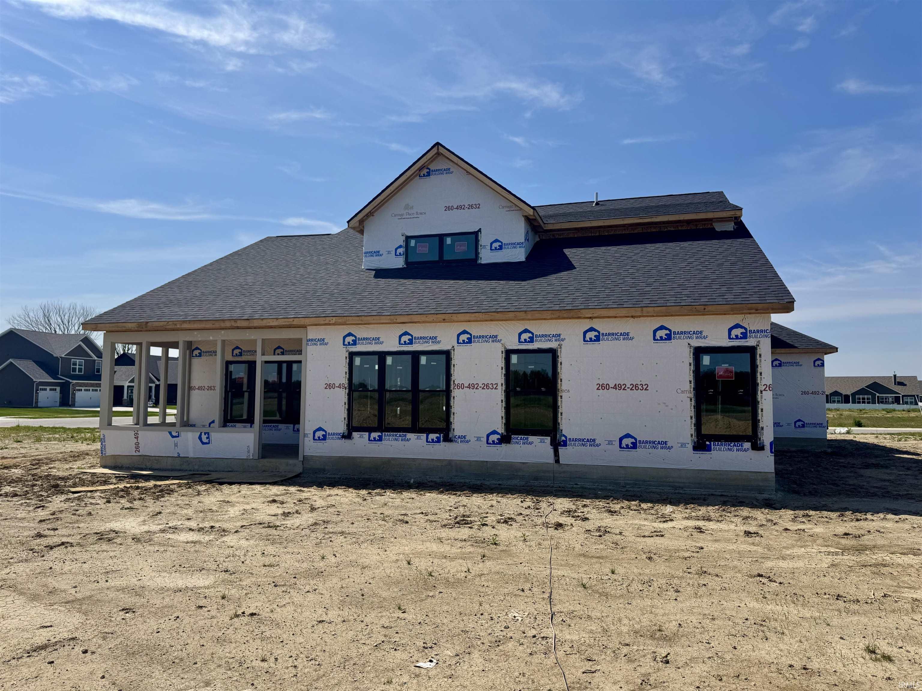 New construction residential structure featuring a dark shingle roof, multiple black-framed windows, and a partially enclosed porch area