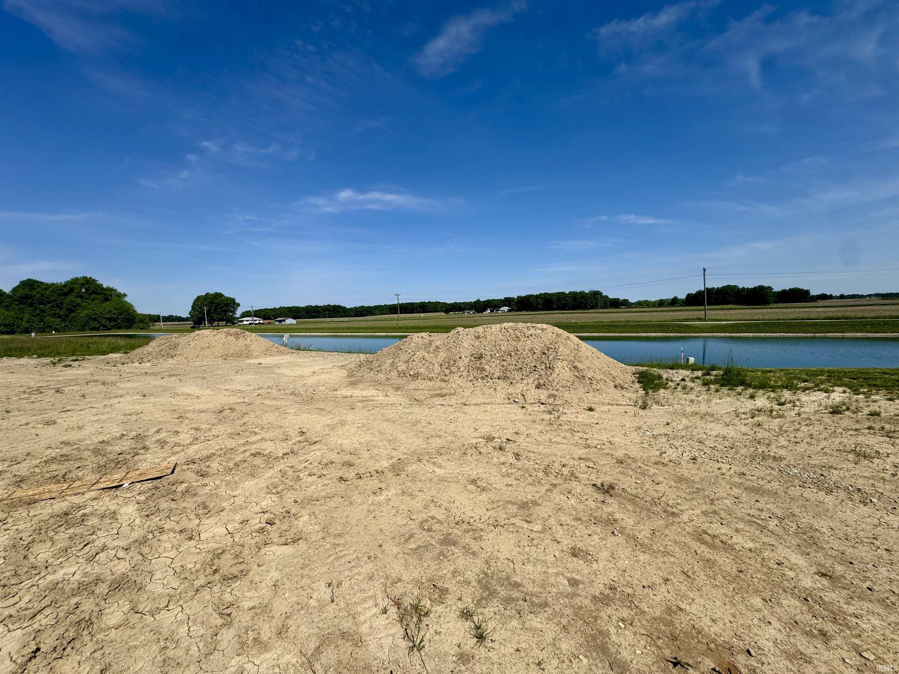Cleared building site featuring excavated earth piles and a water feature