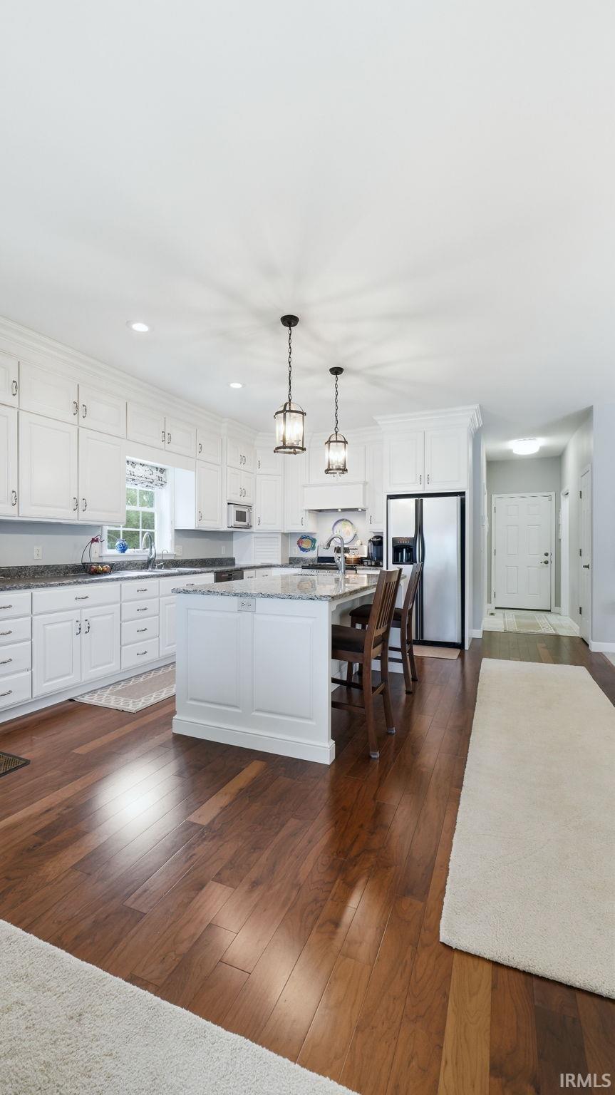 Kitchen featuring wood-finish flooring, white cabinetry, granite countertops, and a center island with seating