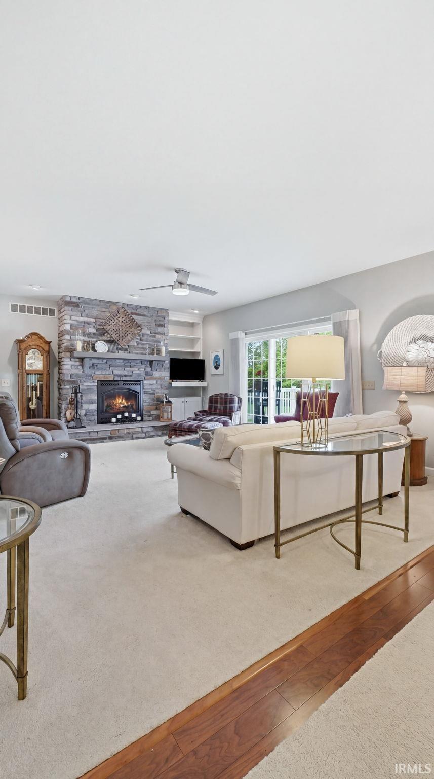 Living area featuring a stone-clad fireplace, built-in shelving, ceiling fan, and carpeted flooring