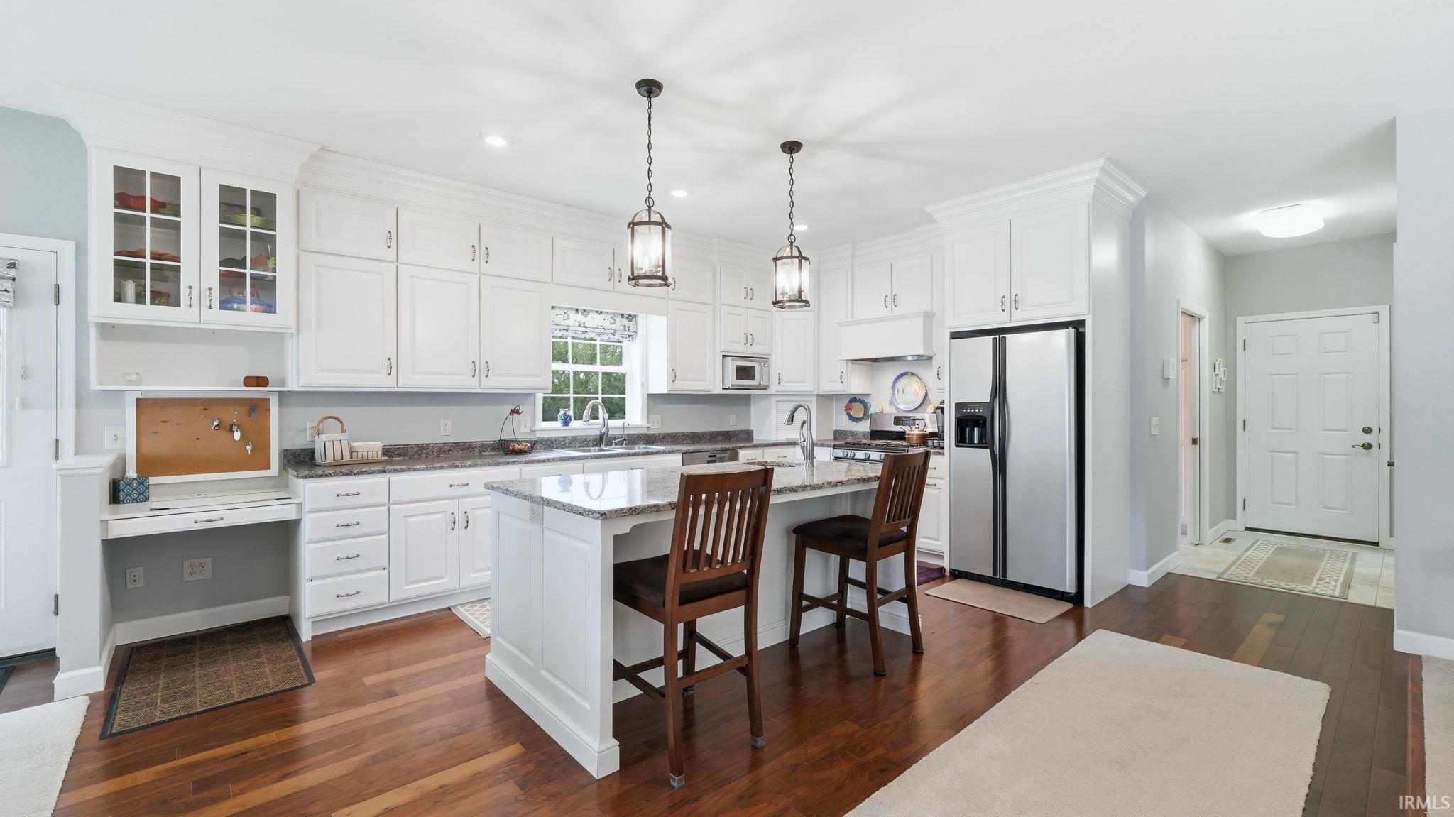 Open-concept kitchen featuring white cabinetry, an island with seating, pendant lighting, stainless steel appliances, and wood-finish flooring