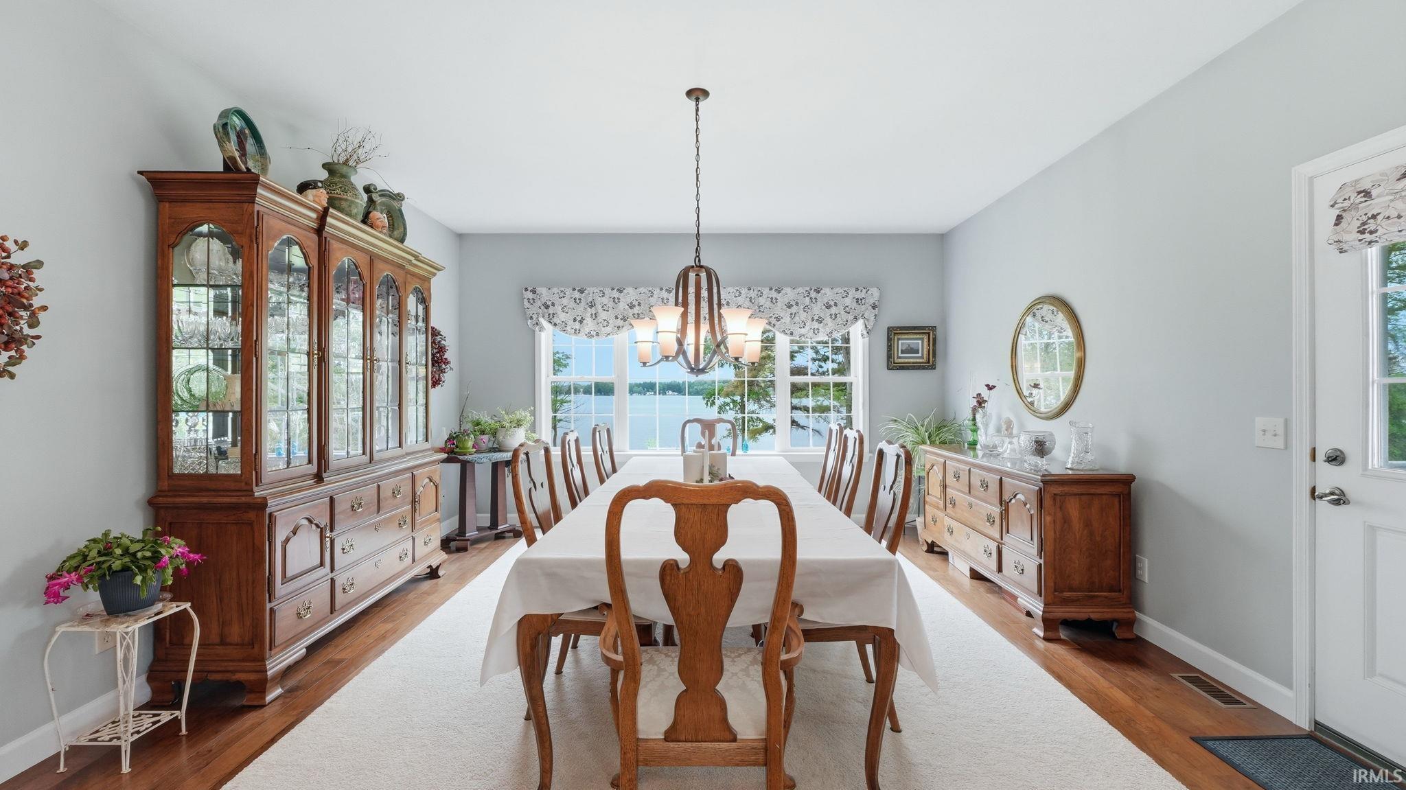 Dining area with expansive lake scenery through large windows, wood-finish flooring, and a central chandelier