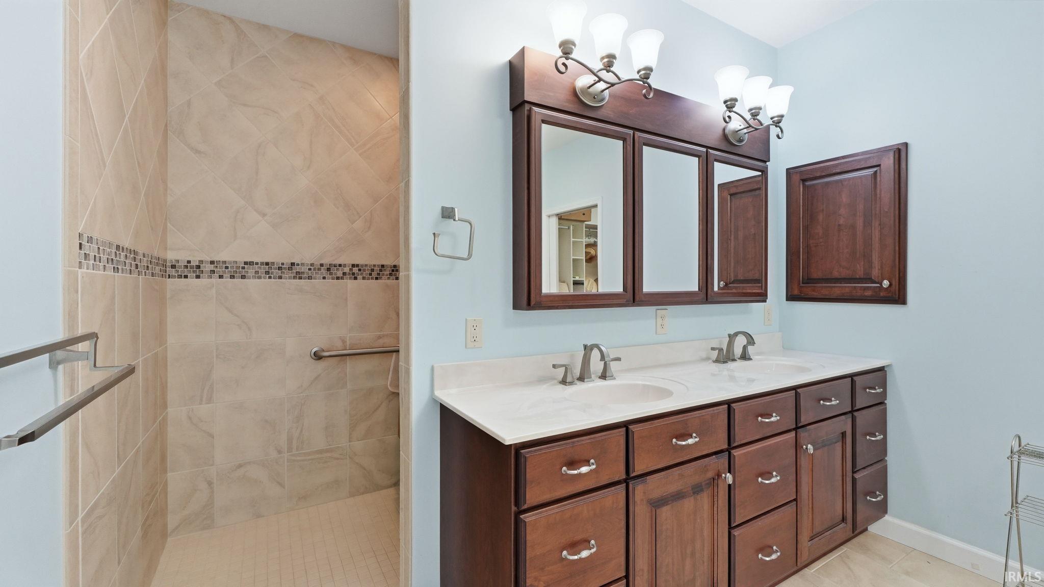 Bathroom featuring a double vanity with stone countertops and undermount sinks, wood-finish cabinetry, and a walk-in shower with tile surround and mosaic accent band
