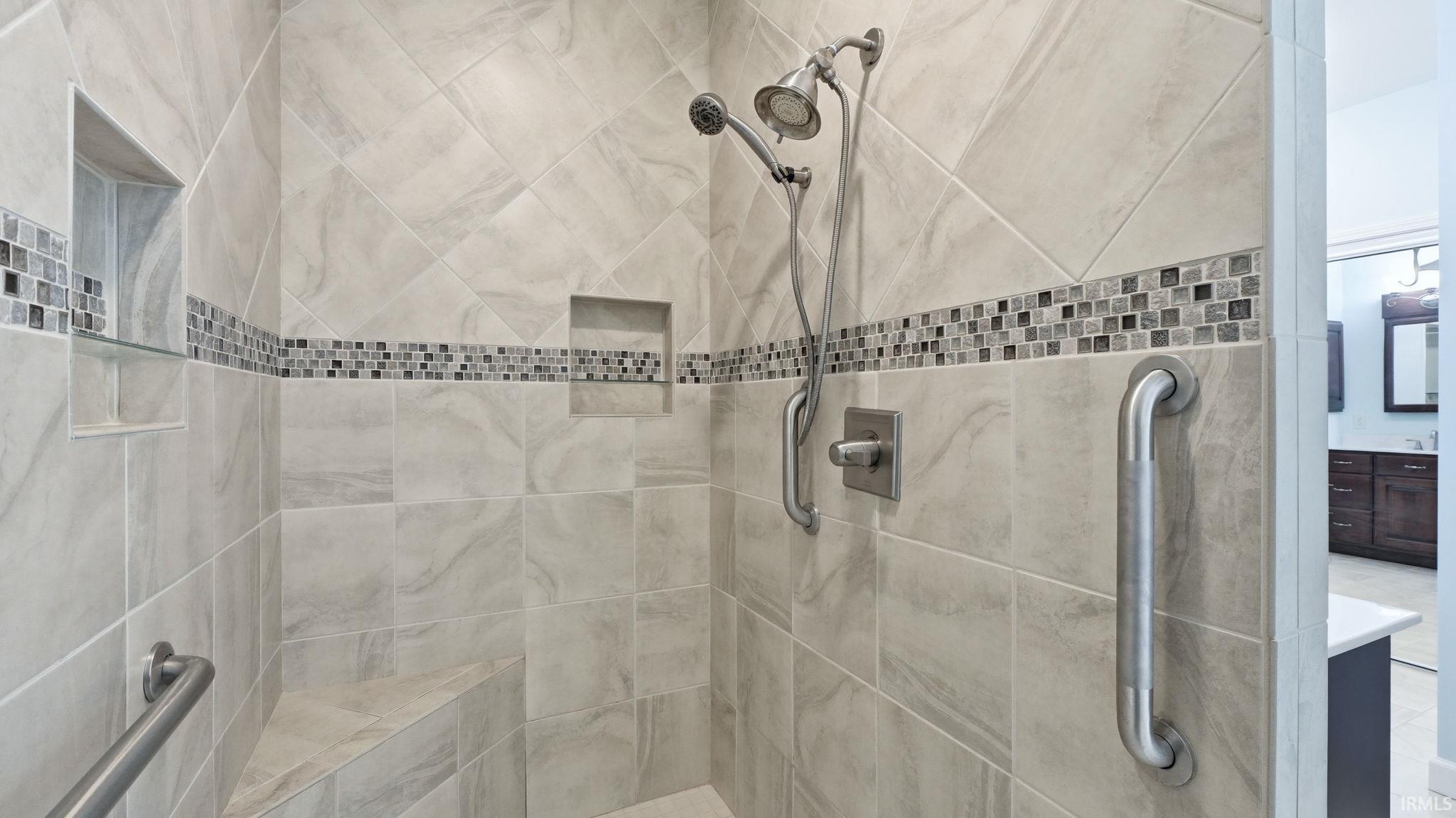 Walk-in shower featuring light-toned tile, a decorative mosaic tile band, two recessed niches, a built-in bench, and grab bars