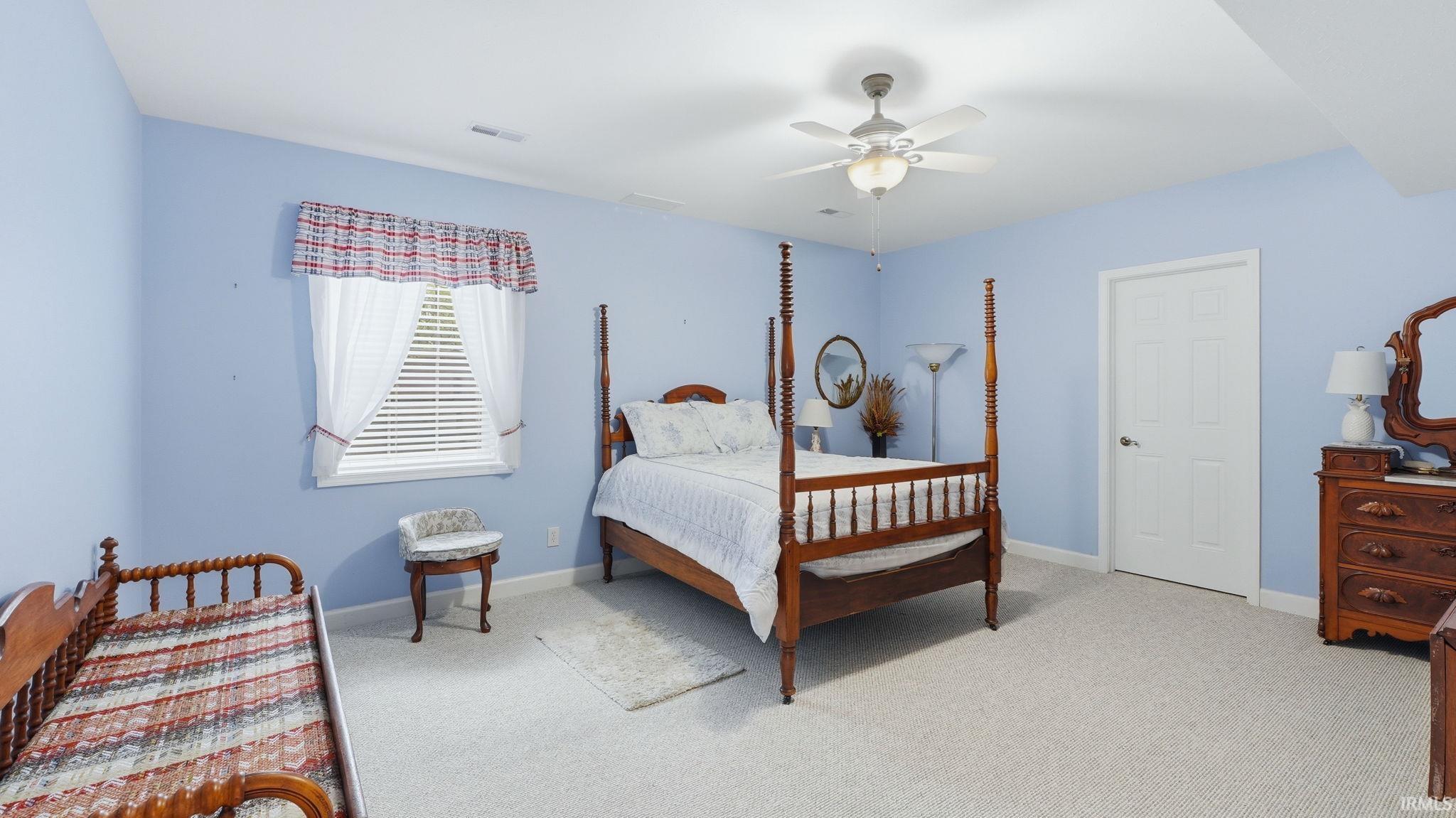 Carpeted interior room featuring light blue walls, a ceiling fan with integrated lighting, a white paneled door, and a single window with white blinds
