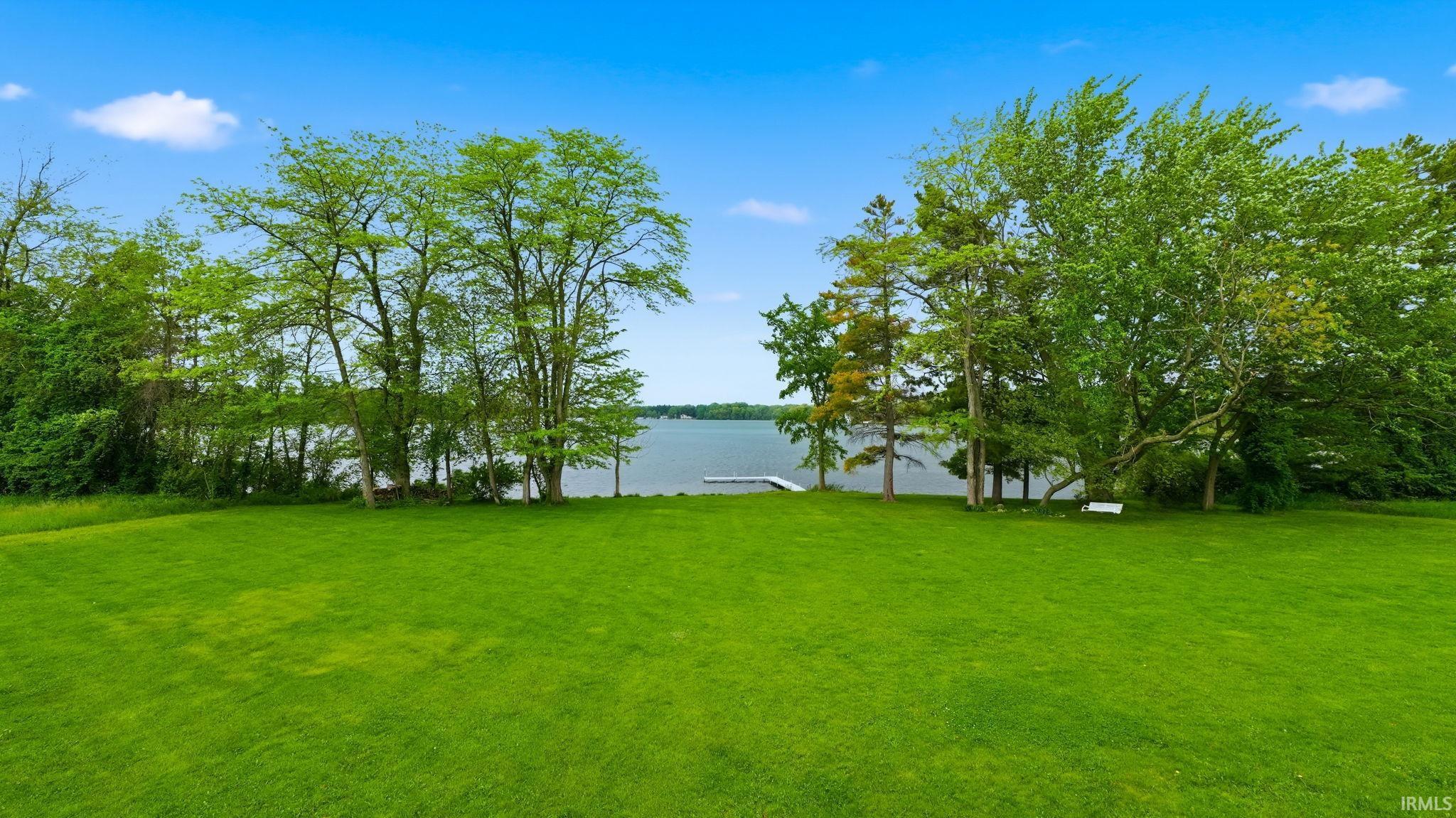 Expansive waterfront lawn featuring mature trees and a private dock leading to the water