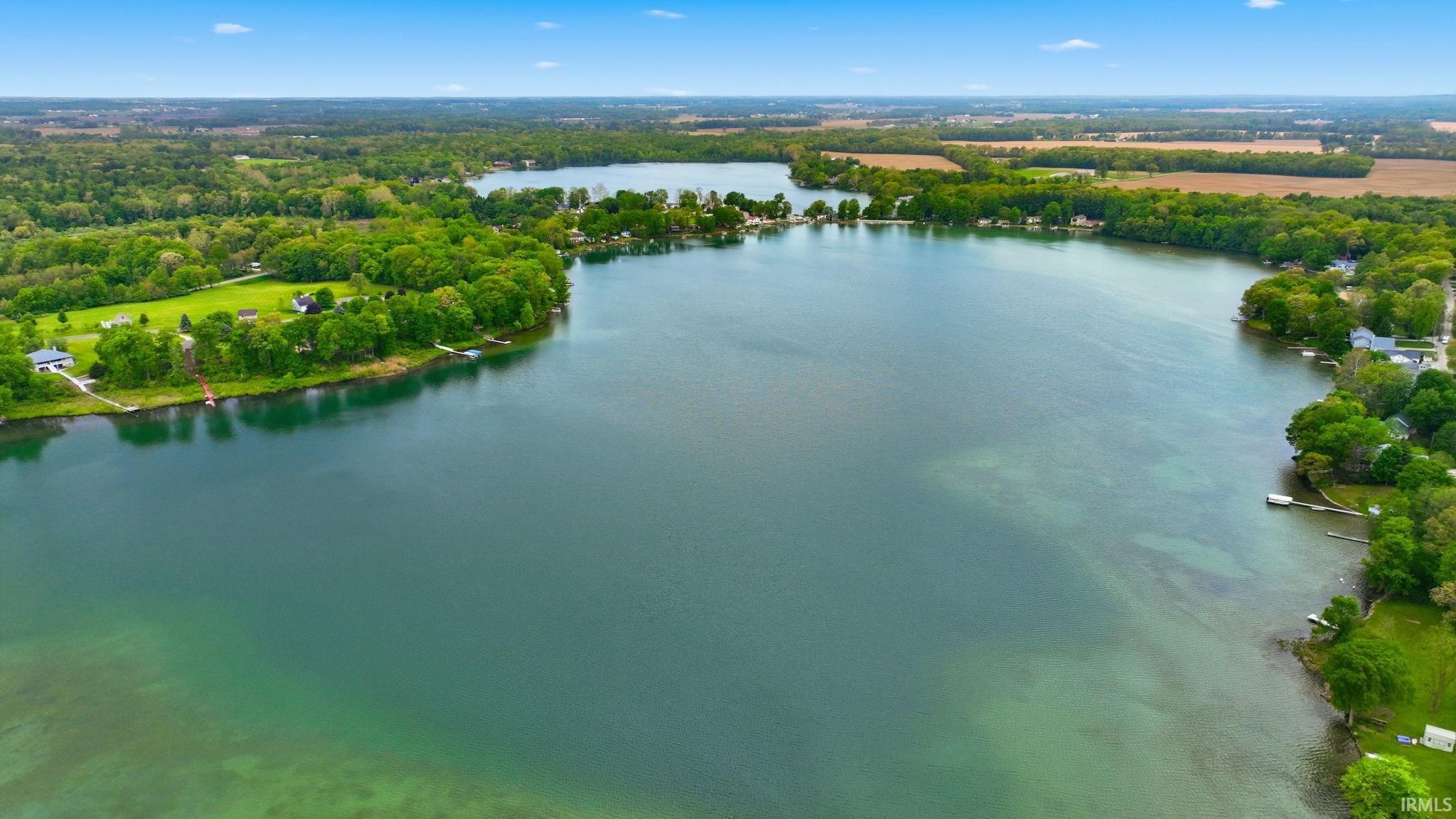 Expansive lakefront property featuring a broad body of water, surrounding mature trees, and a clear blue sky