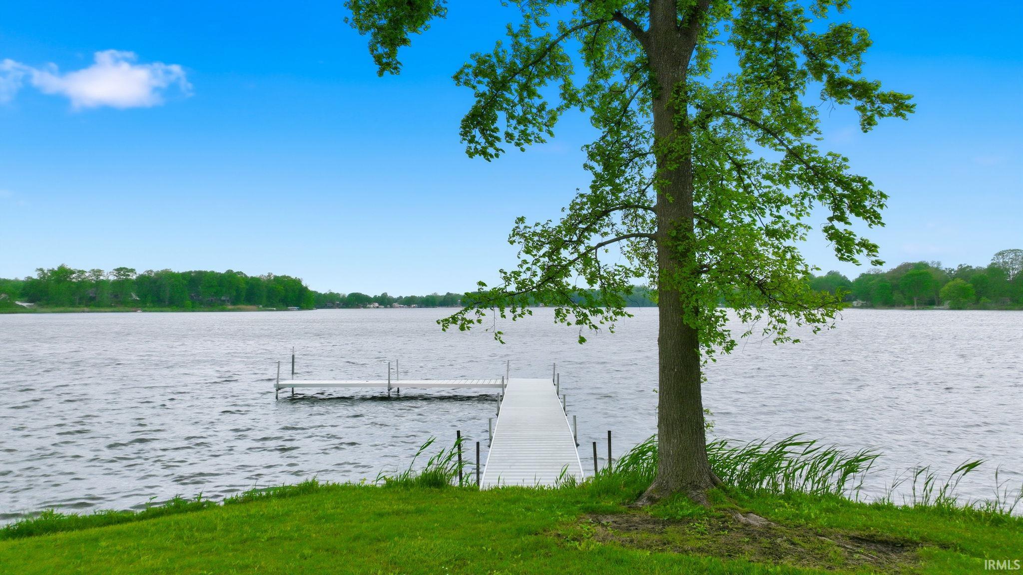 Waterfront property featuring a private dock, expansive water frontage, established tree, and a manicured lawn