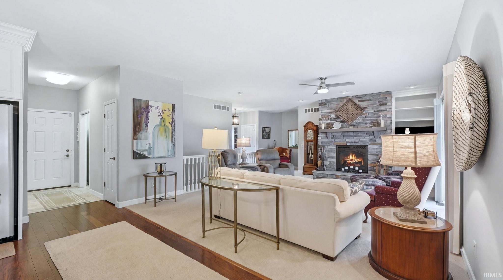 Spacious living area featuring a stone-faced fireplace, built-in shelving, wood-finish flooring, and a ceiling fan