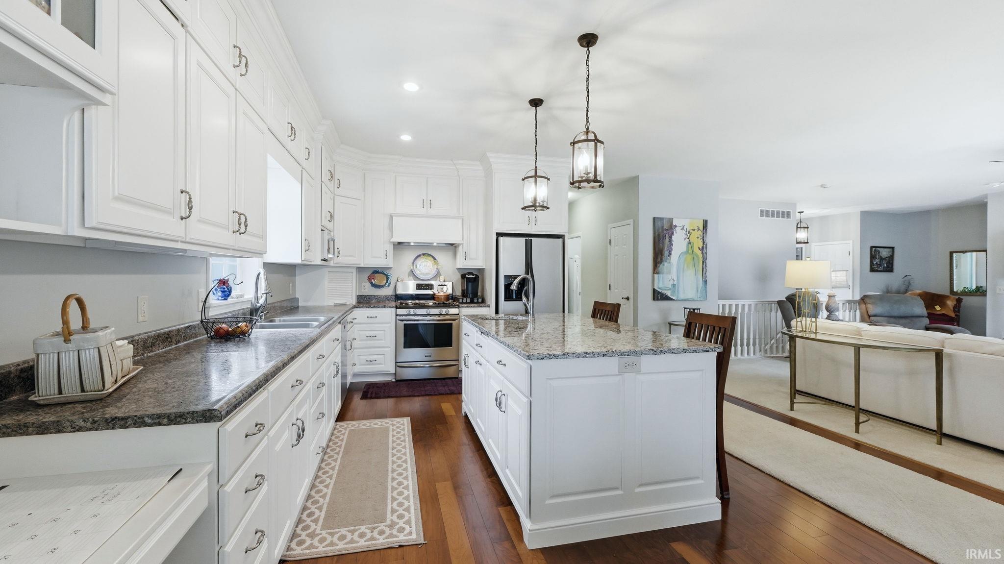 Kitchen featuring white cabinetry, granite countertops, stainless steel appliances, a center island with seating, and wood flooring