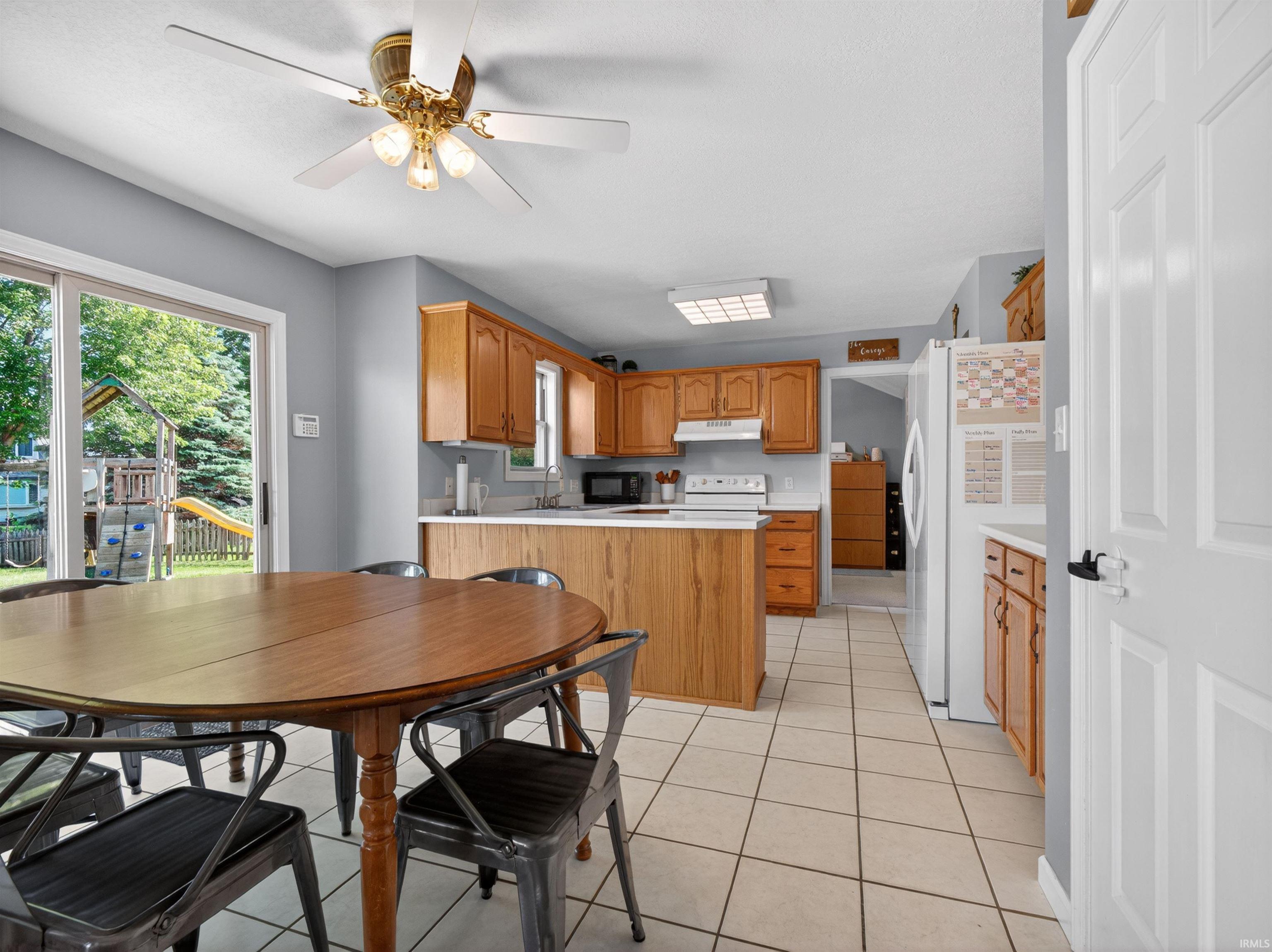 Kitchen and dining area featuring a sliding glass door, overhead ceiling fan, wood-finish cabinetry, white countertops, and tile flooring
