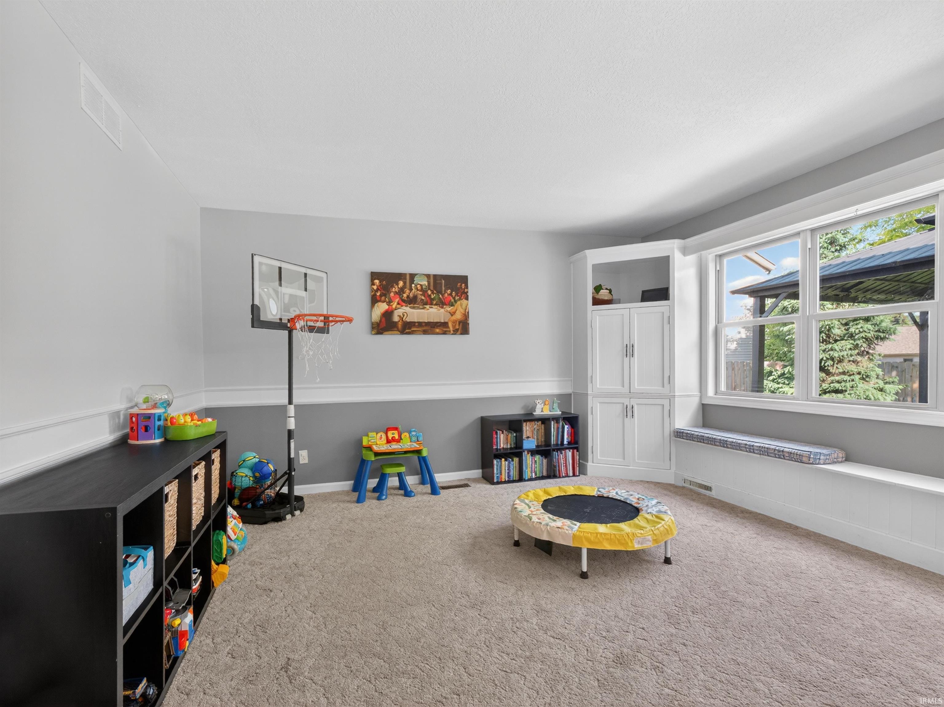 Carpeted room featuring a large bay window with a built-in window seat, a built-in white cabinet with shelving, and two-tone painted walls with chair rail molding