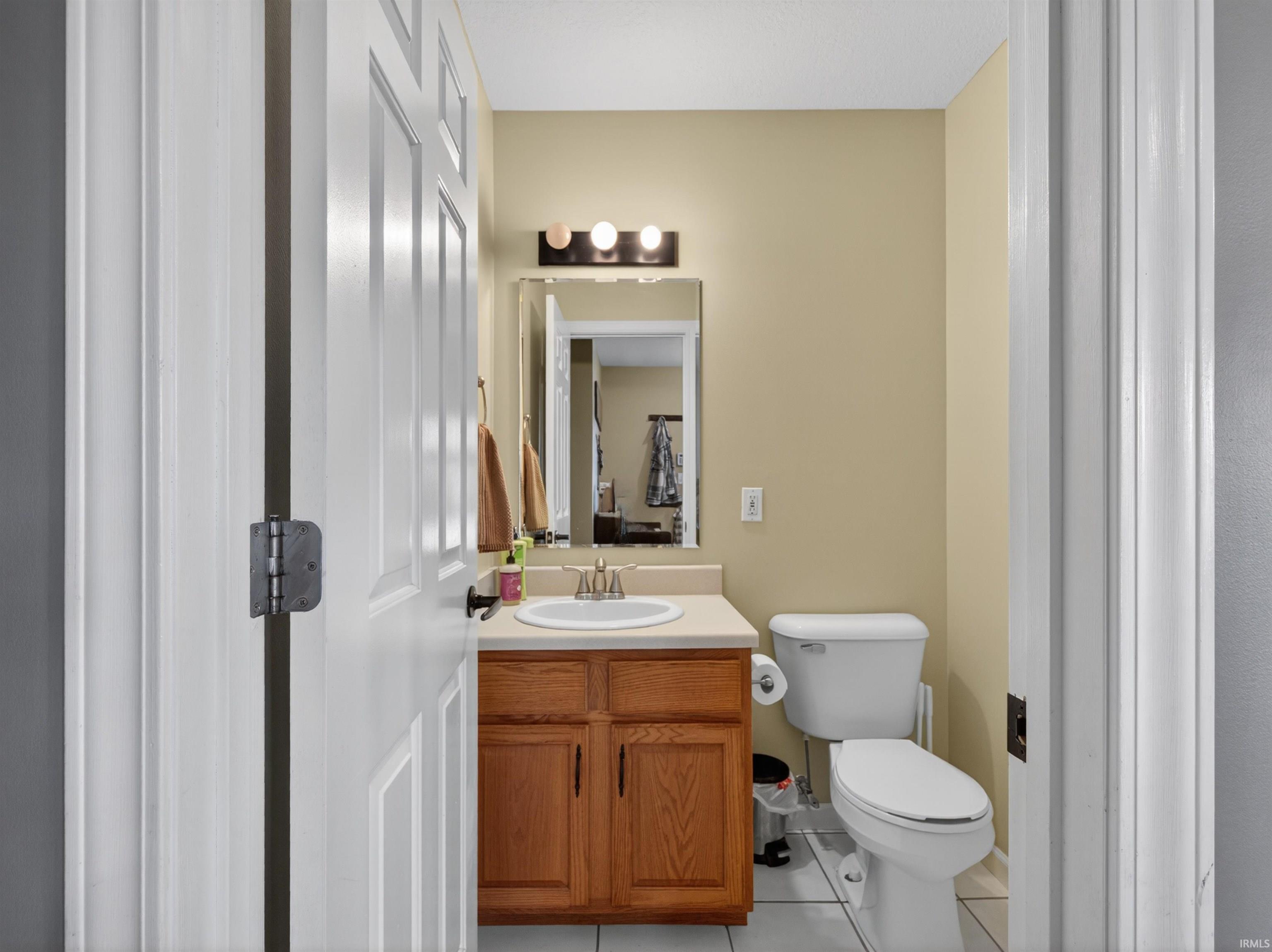 Compact bathroom featuring a single vanity with wood-finish cabinetry, a white countertop, and a rectangular mirror with a three-light fixture