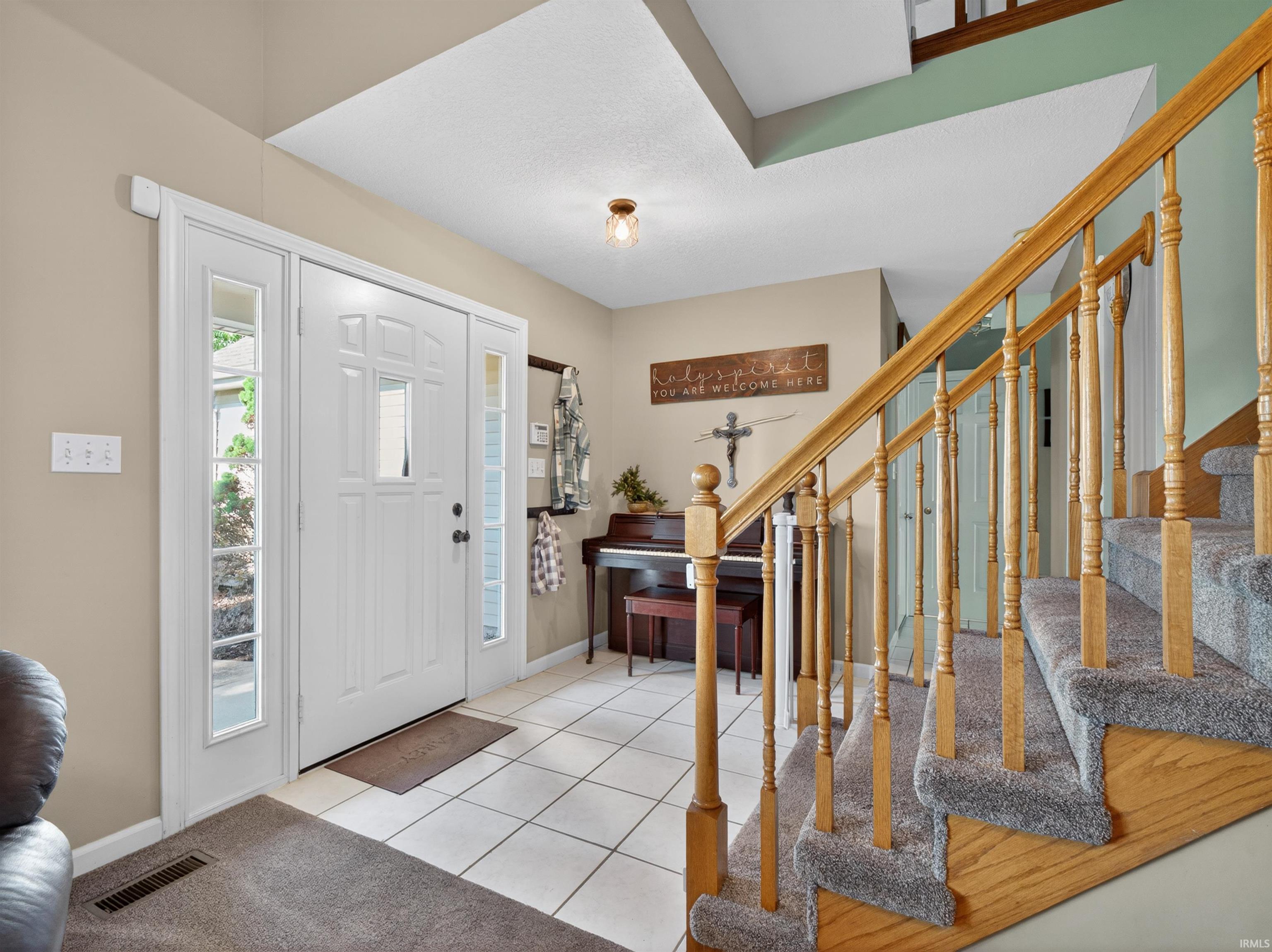 Entryway featuring a paneled door with side lights, ceramic tile flooring, and a carpeted staircase with wood balusters and handrail