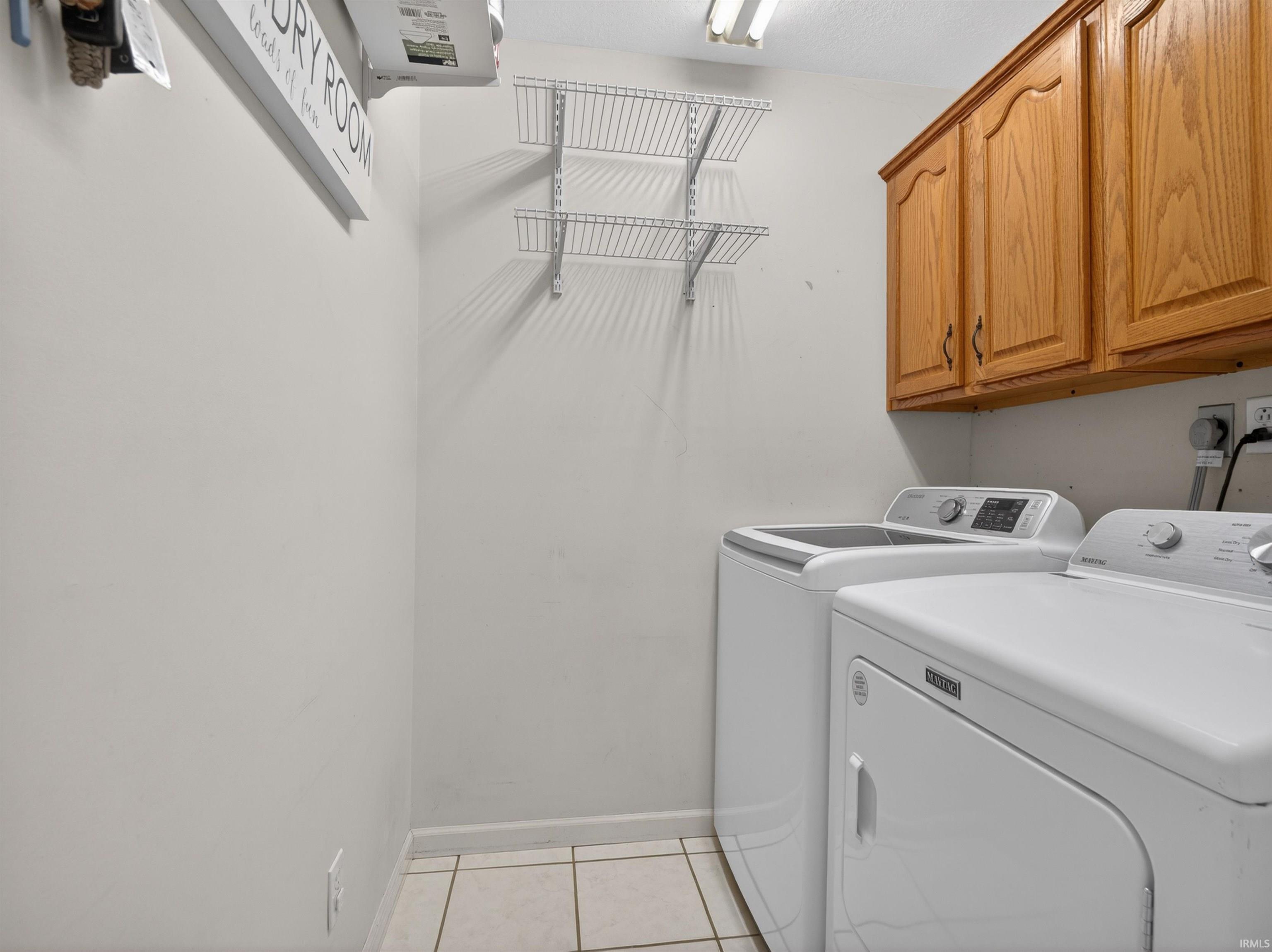 Utility space featuring light wood cabinetry, white tile flooring, and wall-mounted wire shelving