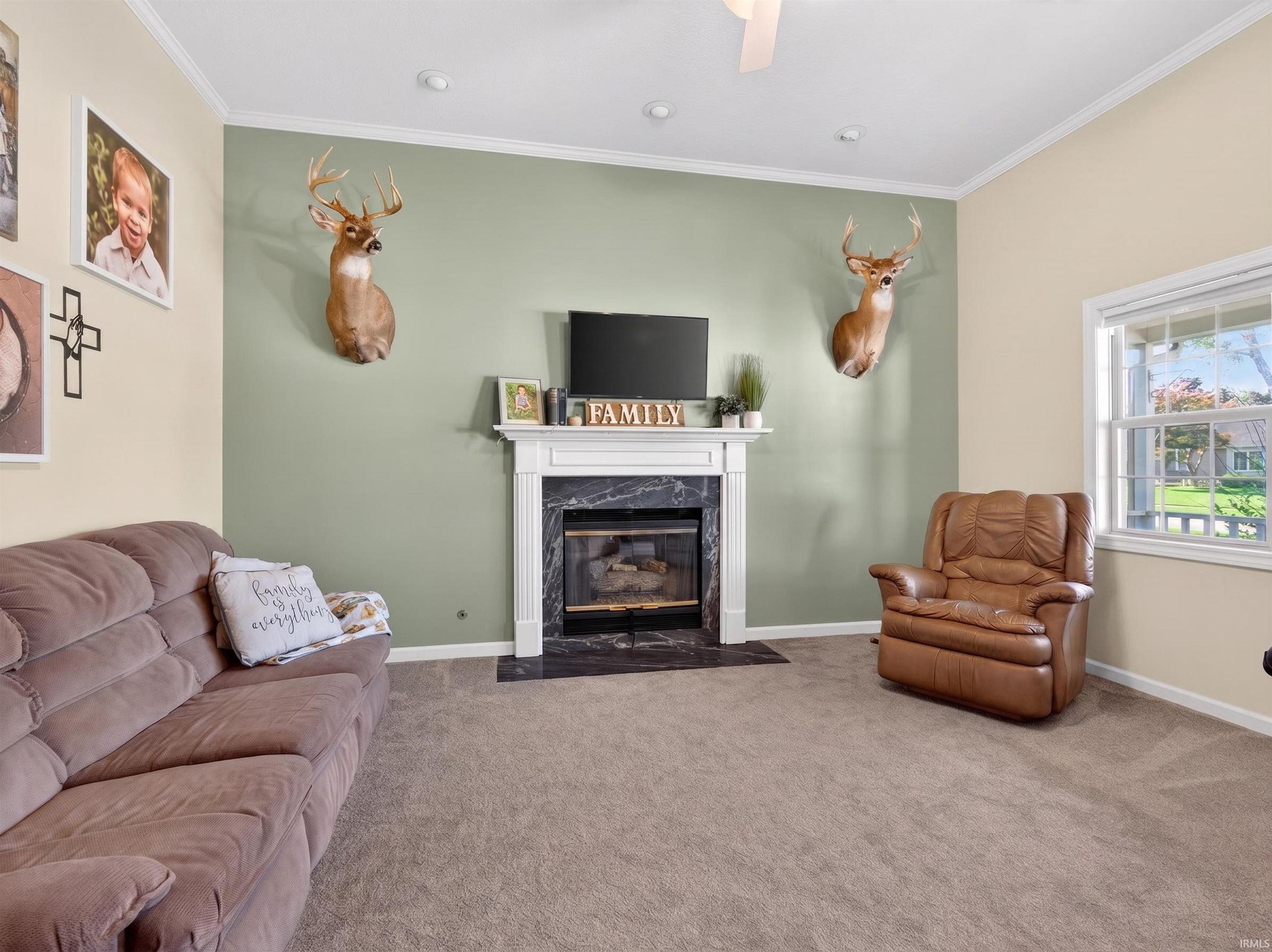 Living area featuring a fireplace with a white mantel and dark stone surround, recessed lighting, crown molding, a ceiling fan, and a window providing natural light