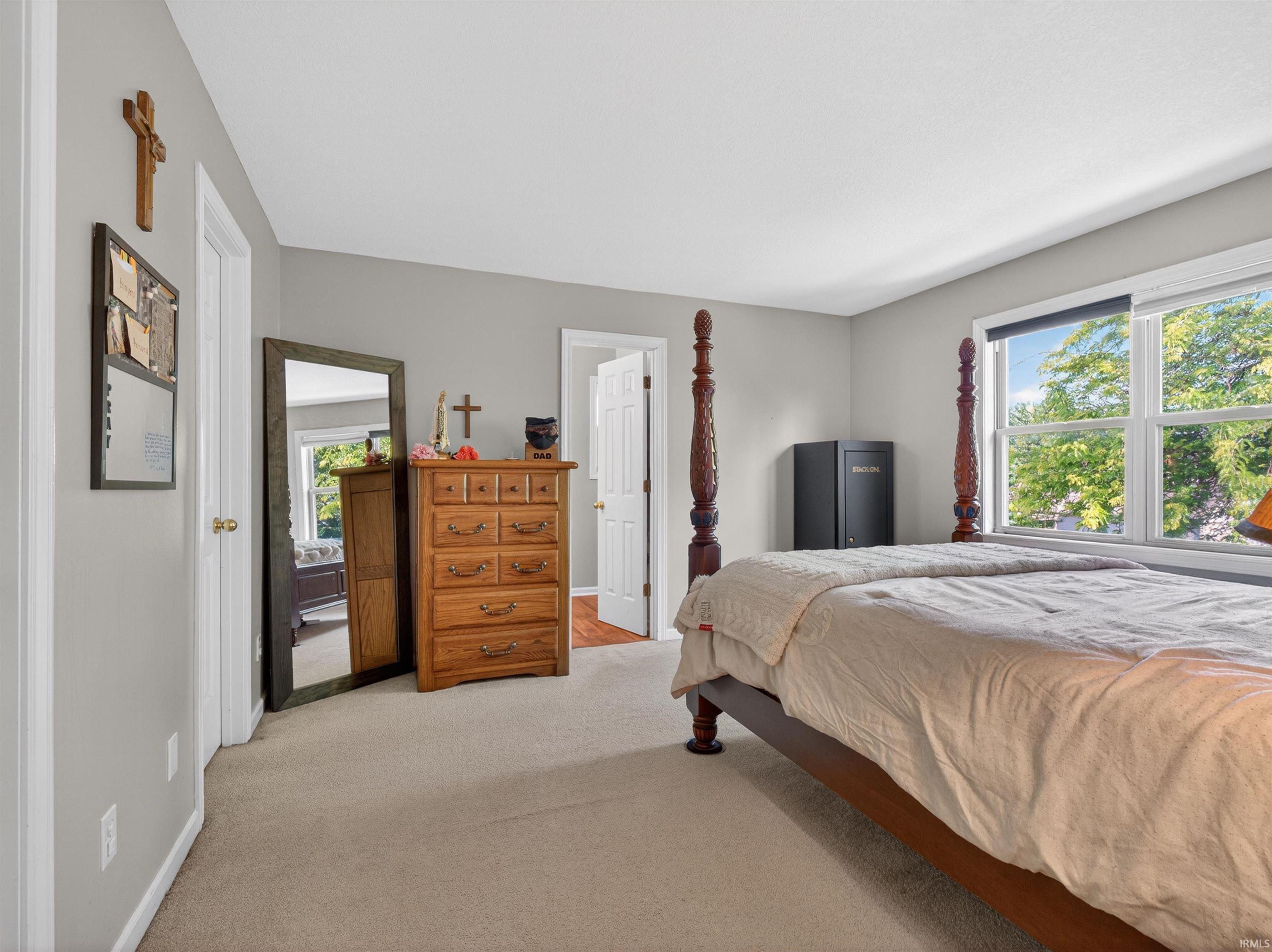 Carpeted bedroom featuring light gray walls, white trim, and a large window with exterior foliage