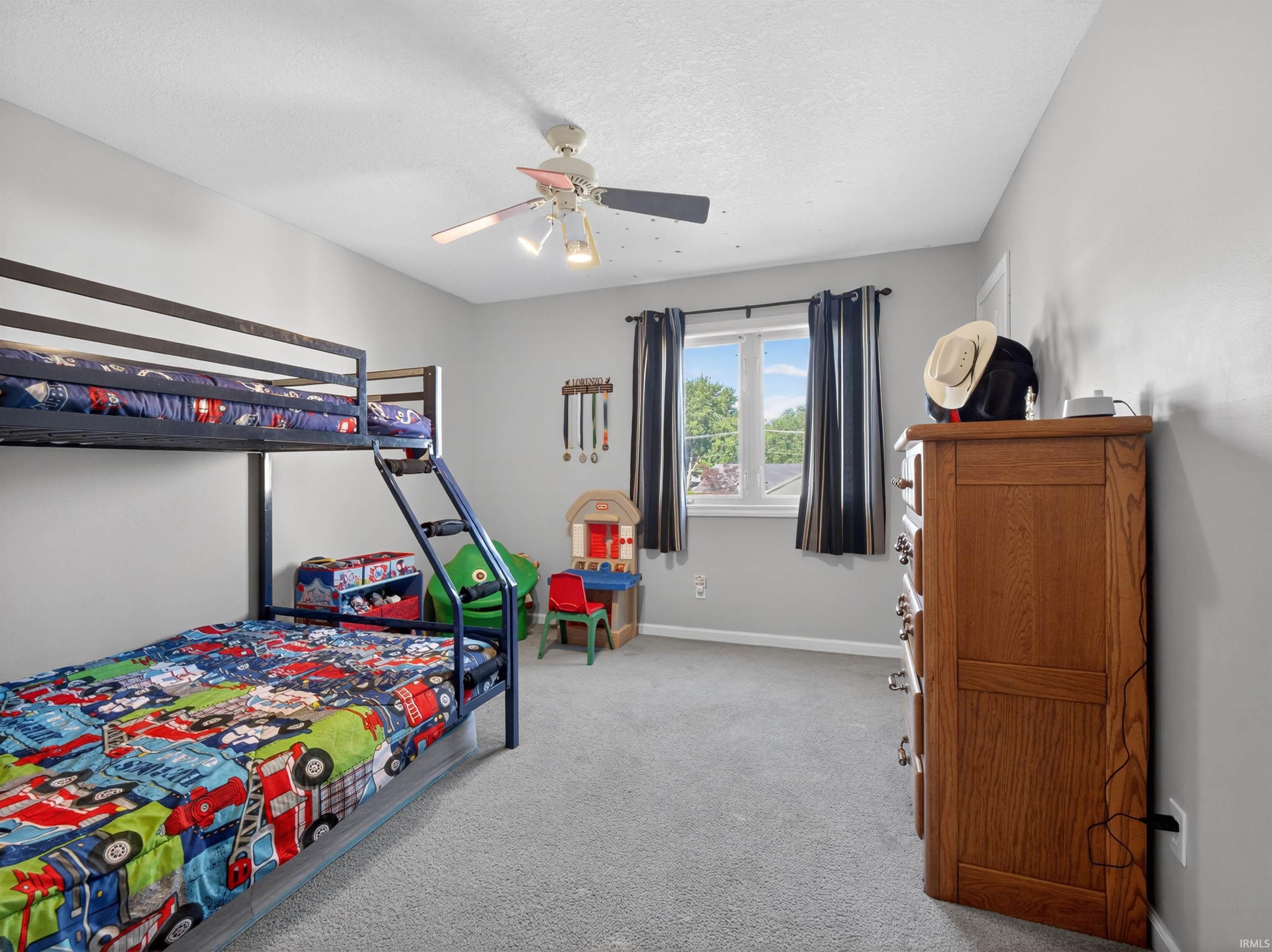 Carpeted room featuring a ceiling fan with light fixture, window with drapes, and light gray walls